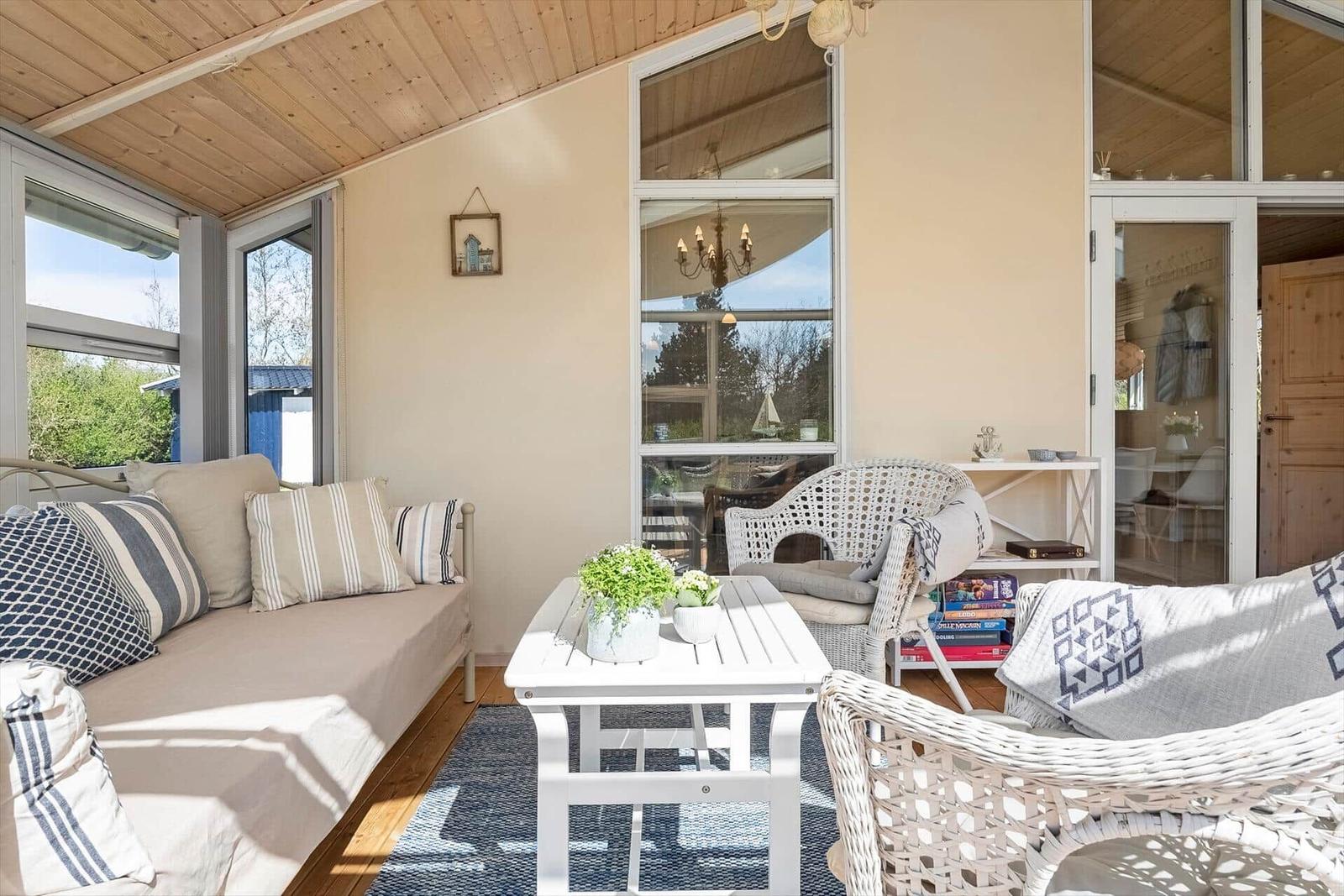 Ein Wohnbereich mit Sofa, Stühlen und Tisch. Große Fenster und Holzdecke.