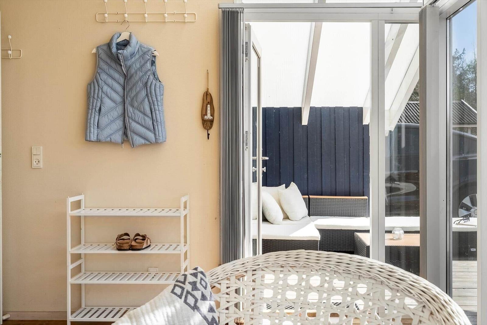 Ein Raum mit Schuhregal, Jacke und Blick auf eine Terrasse mit Sitzmöbeln.