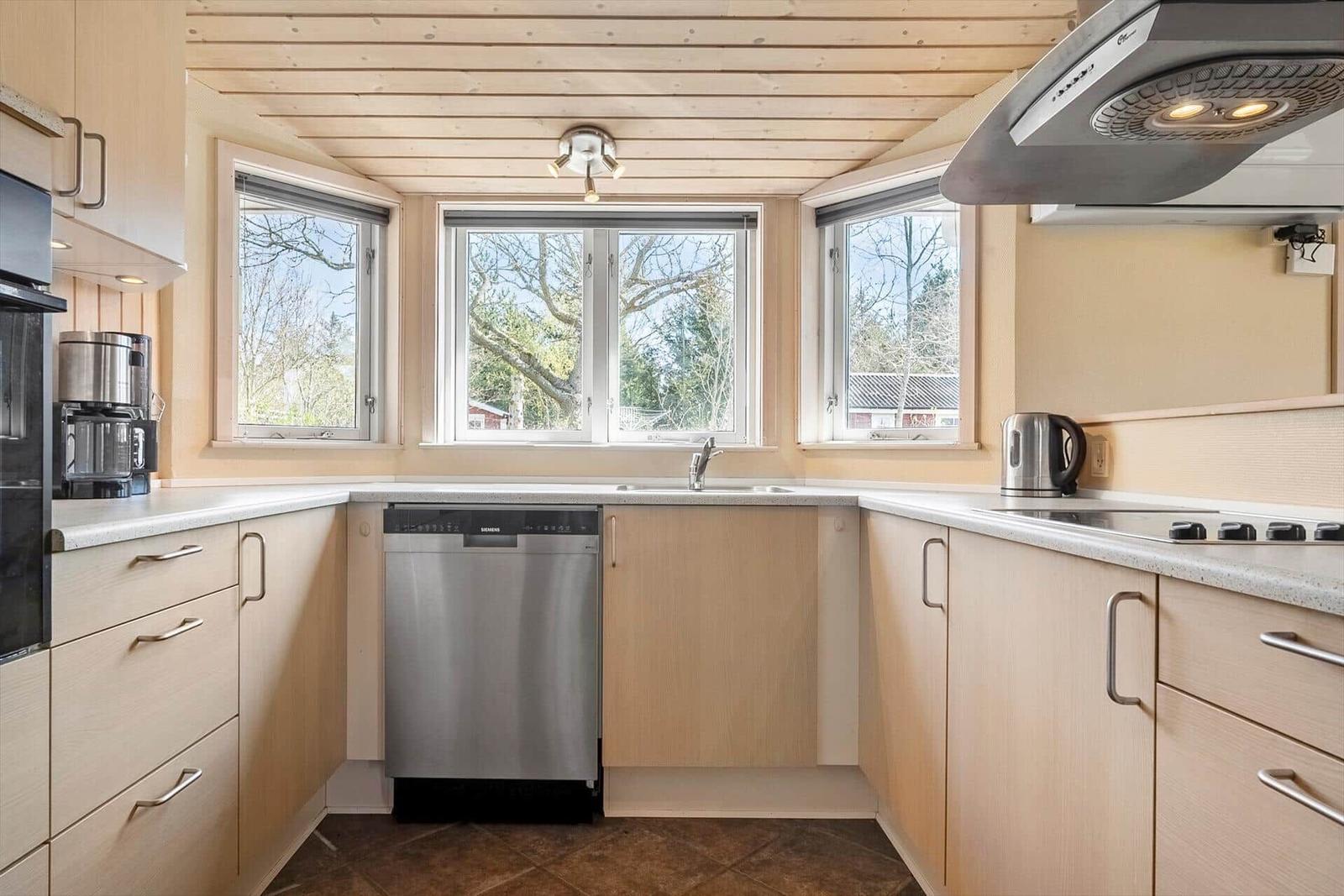 Küche mit Holzdecke, Fenstern und moderner Geräteausstattung.