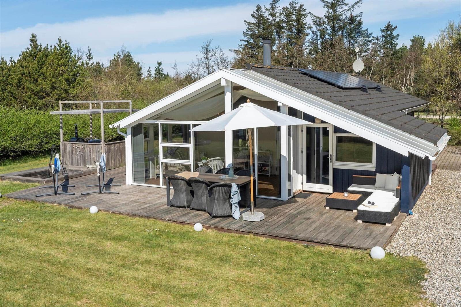 Haus mit Terrasse, Grillplatz und Garten. Weiße Sonnenschirme und Sitzgelegenheiten.