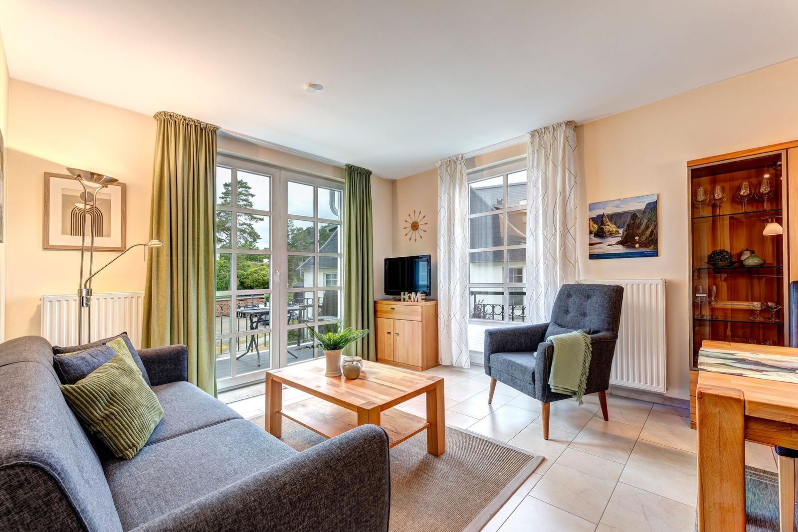 Wohnzimmer mit Sofa, Sessel, Couchtisch und Fenstern zur Terrasse.