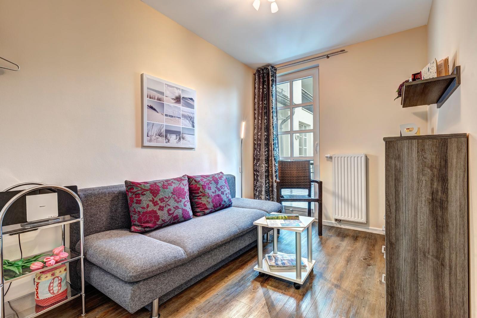 Ein Wohnzimmer mit Sofa, Tisch und Fenster. An der Wand hängt ein Bild.