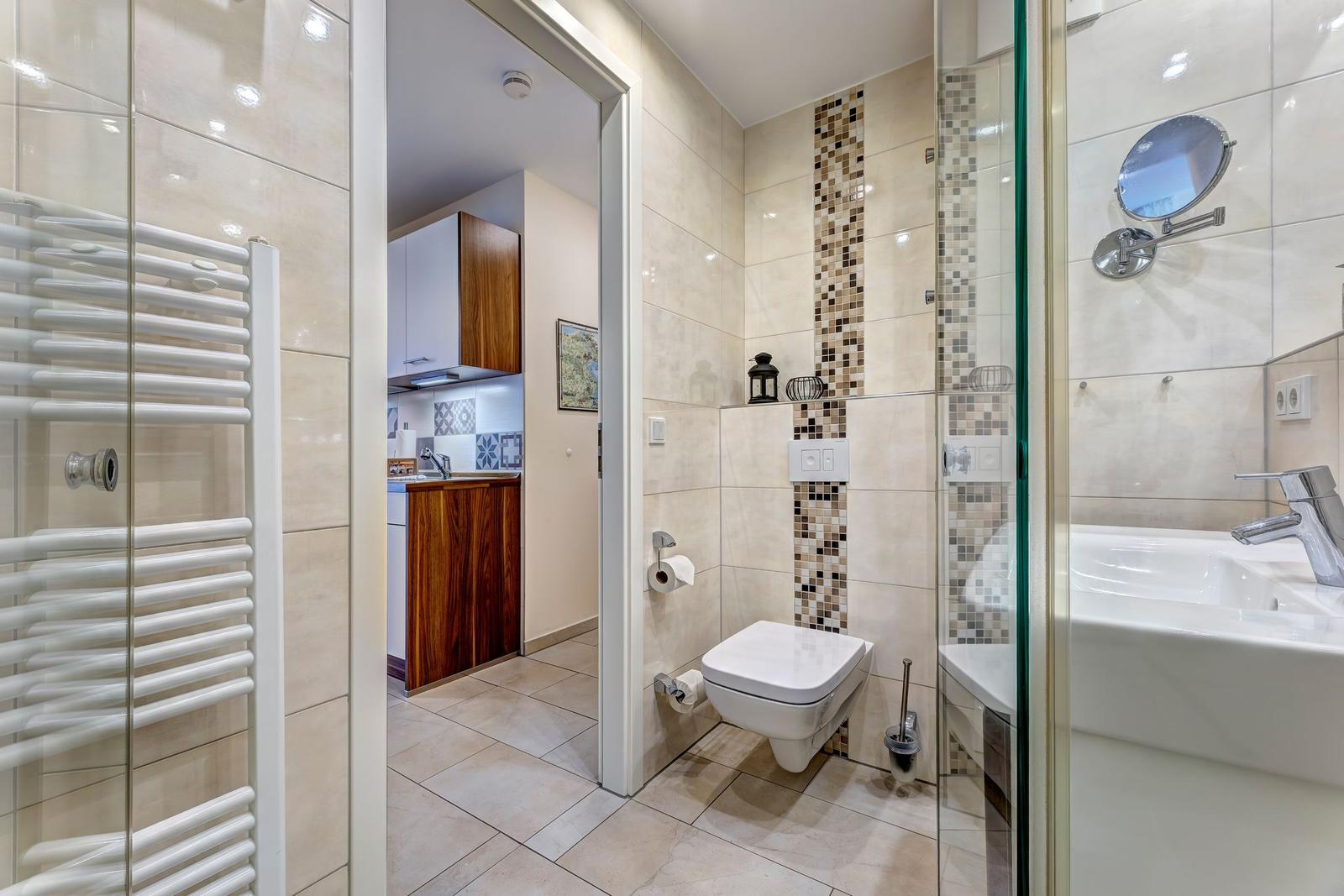 Badezimmer mit Toilette, Dusche und Heizkörper. Küche im Hintergrund sichtbar.