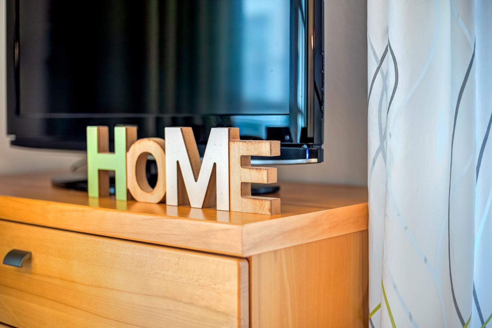 Holzfiguren mit dem Wort HOME stehen vor einem Fernseher auf einem Schrank.