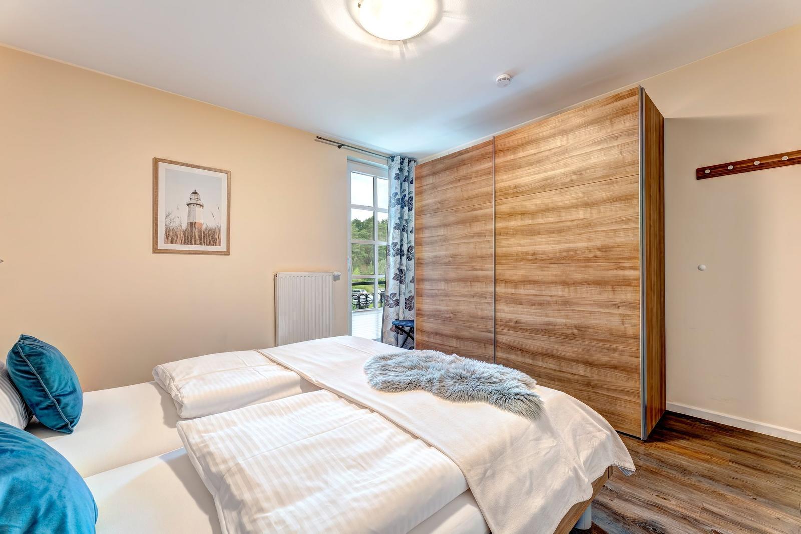 Schlafzimmer mit Doppelbett, Holzschrank und Fenster zum Balkon.