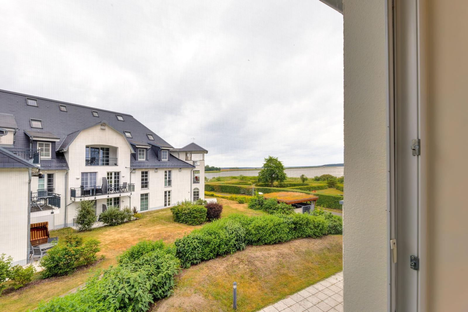Blick auf ein weißes Gebäude mit Balkonen und grüne Gärten im Vordergrund.