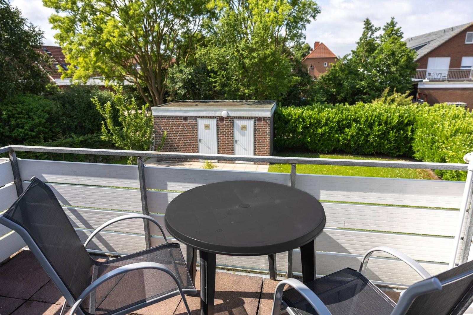 Terrasse mit Tisch und zwei Stühlen. Blick auf grüne Bäume und einen Garten.