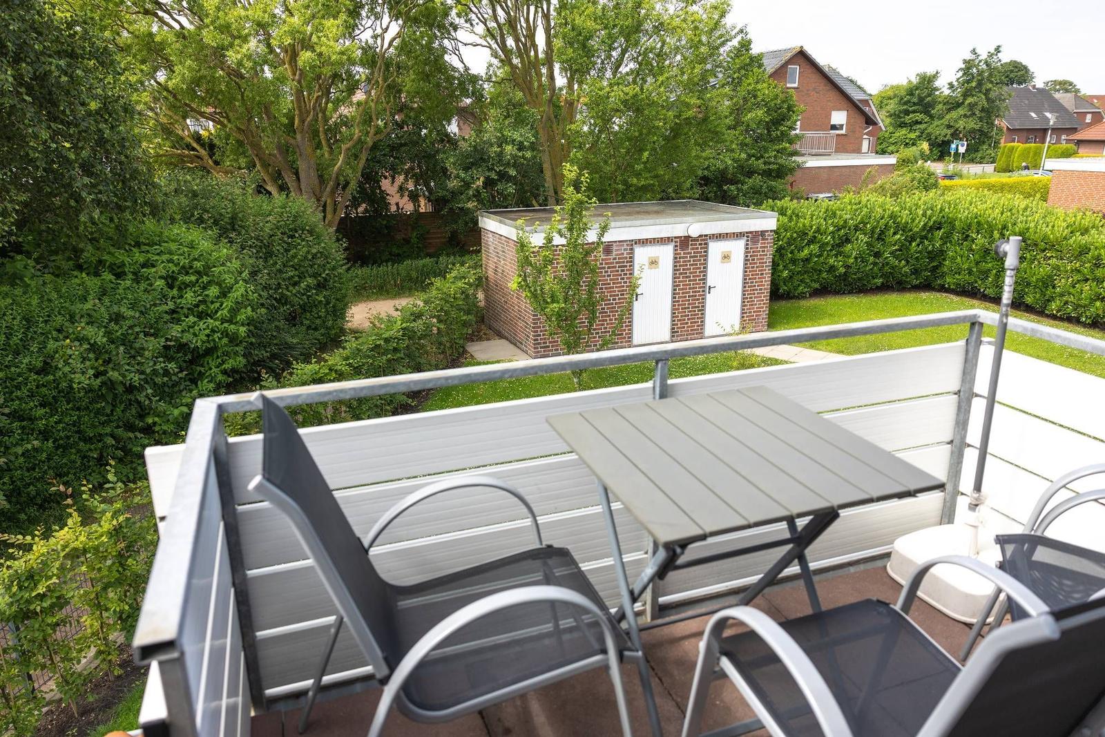 Terrasse mit Tisch und Stühlen, Blick auf grünen Garten und kleines Gebäude.