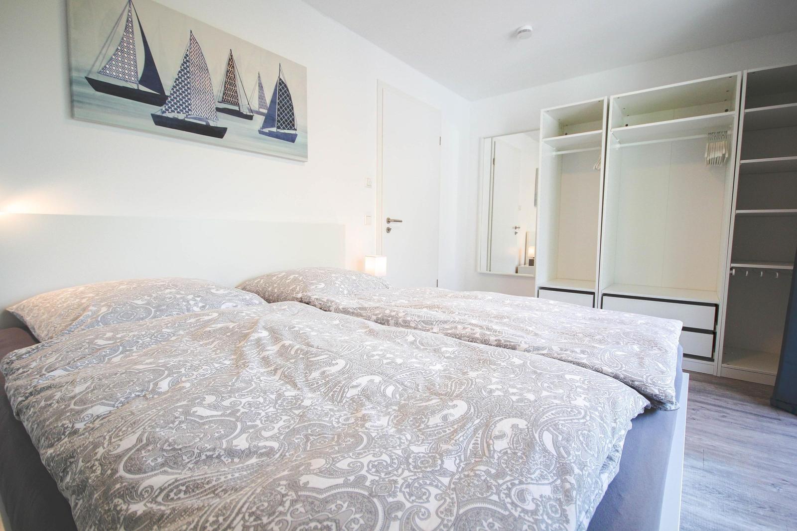 Schlafzimmer mit Doppelbett, Kleiderschrank und Wandbild mit Segelbooten.