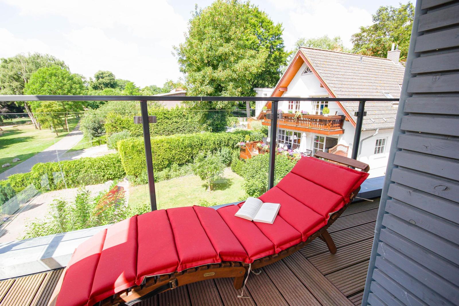 Roter Liegestuhl auf Balkon mit Blick auf Garten und Haus.