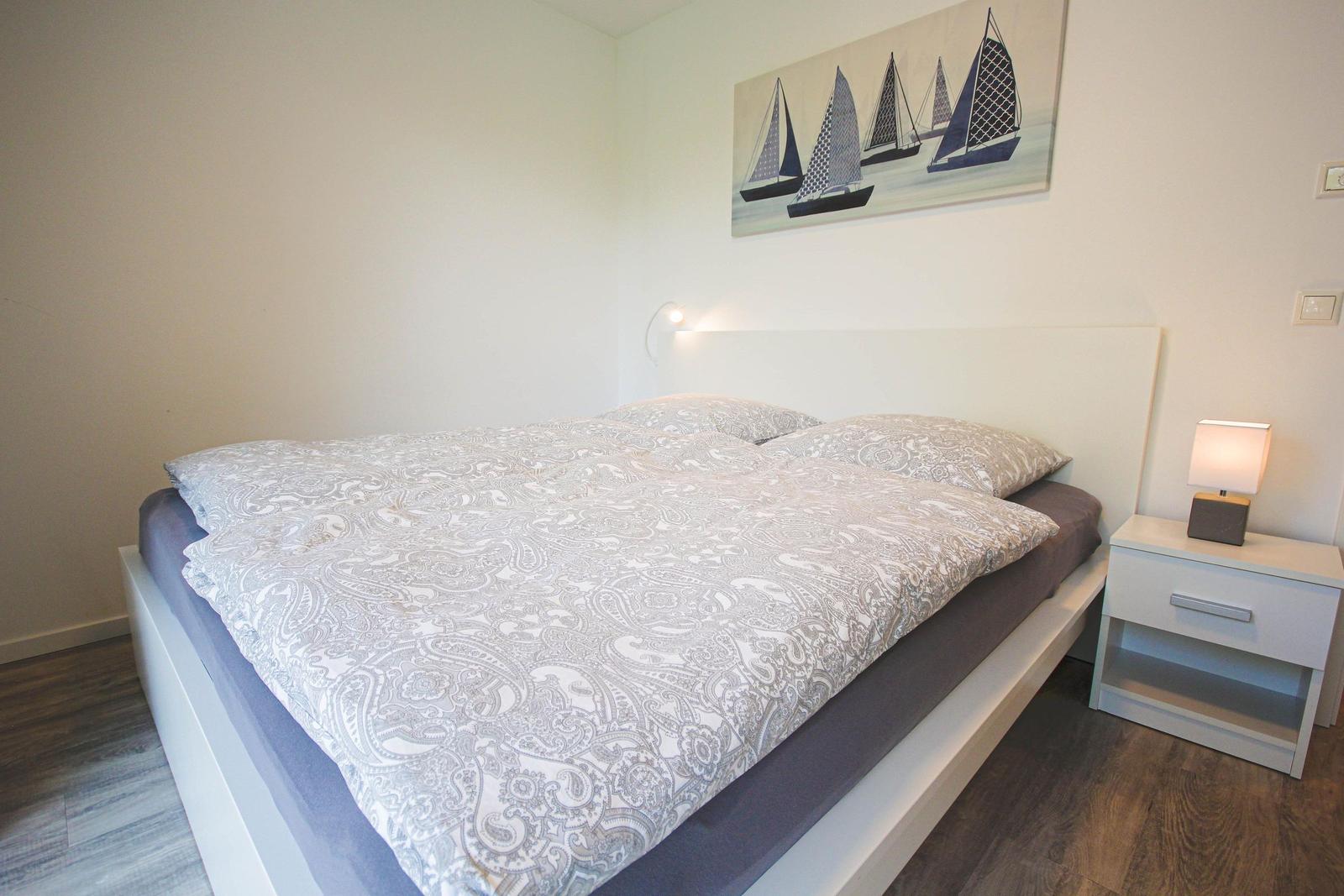 Schlafzimmer mit Doppelbett, Nachttisch und Wandbild mit Segelbooten.