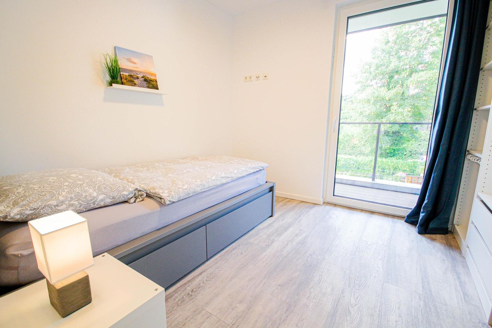 Schlafzimmer mit Bett, Nachttisch und Balkontür.