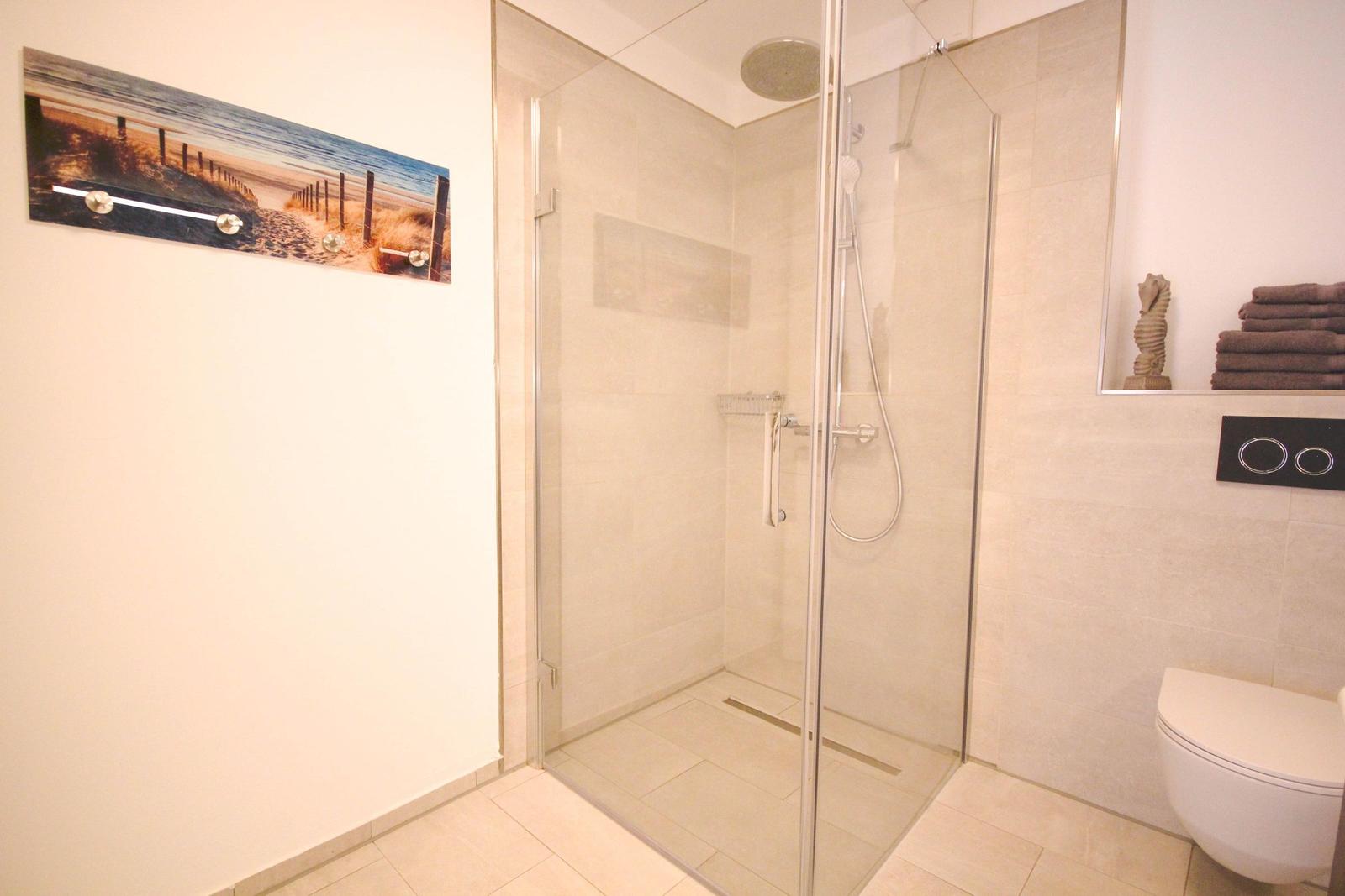 Dusche mit Glaswand, Toilette und Wandbild mit Strandmotiv.