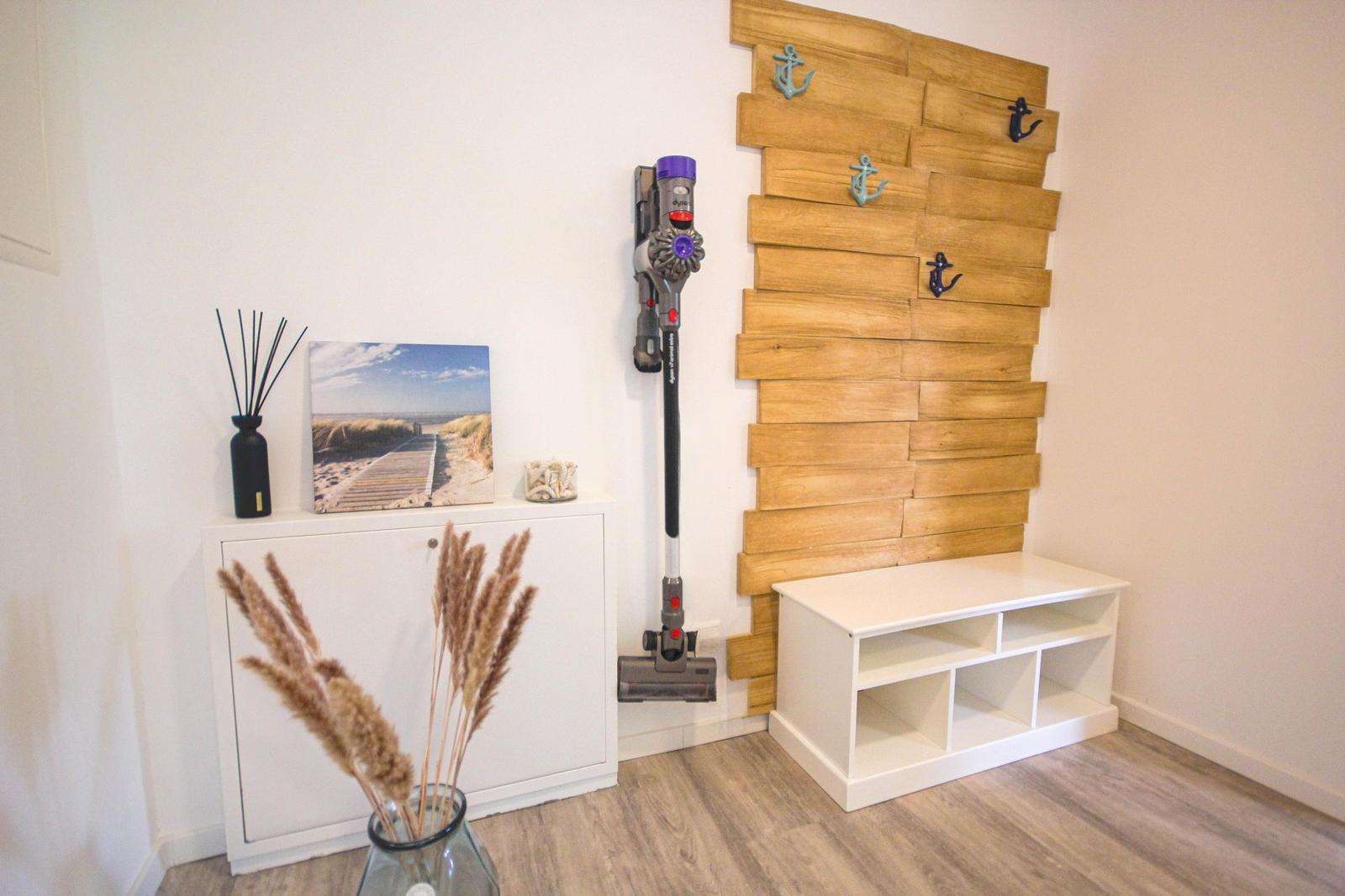 Raum mit Holzwand, Staubsauger, Schrank und Vase mit Pflanzen.