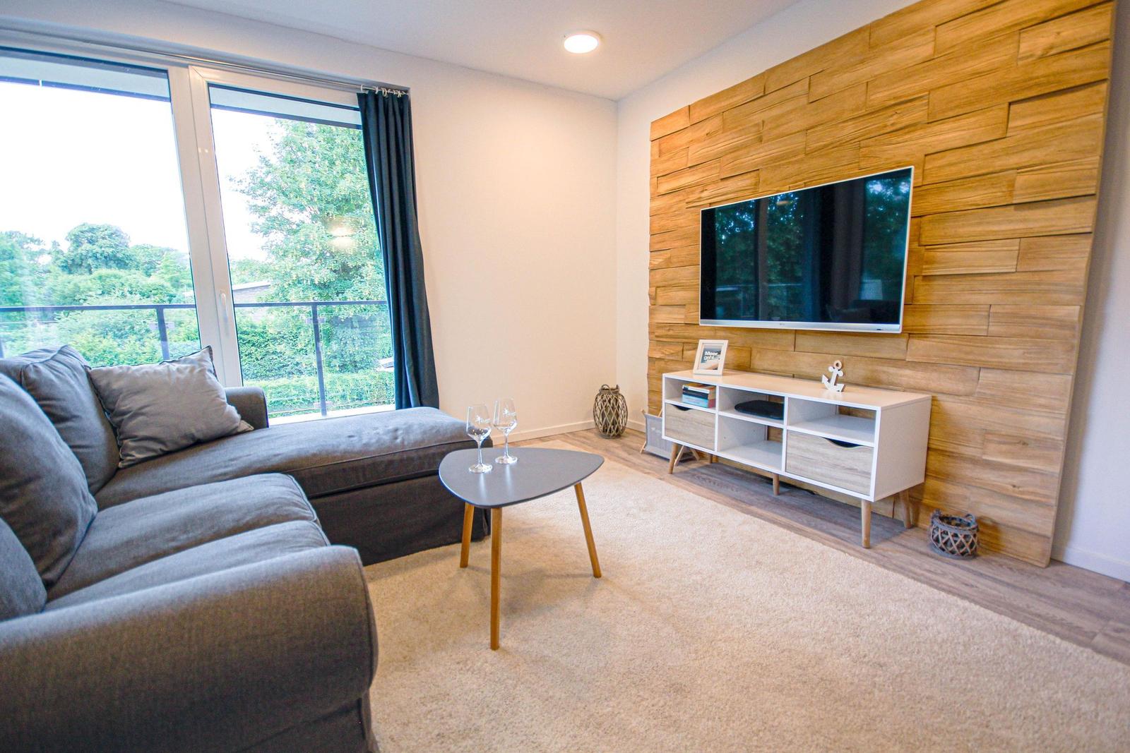 Wohnzimmer mit Sofa, Fernseher an Holzwand und Terrassentür.