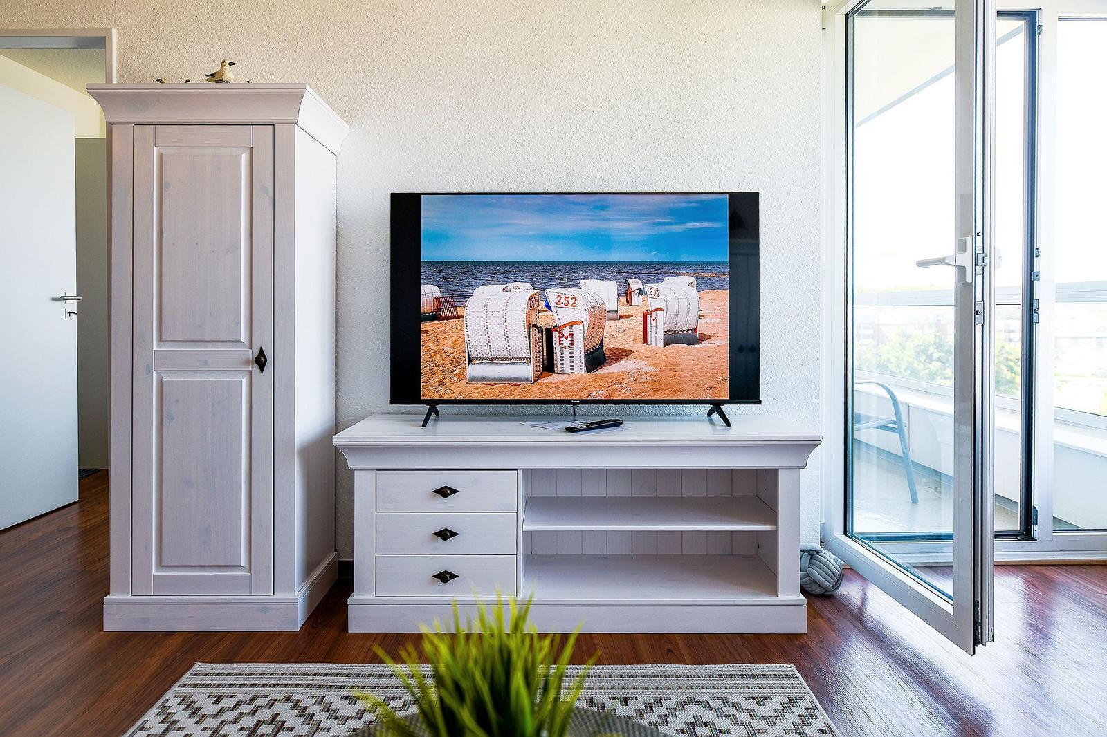 TV auf weißen Möbeln, Blick auf Balkon und Strandbilder