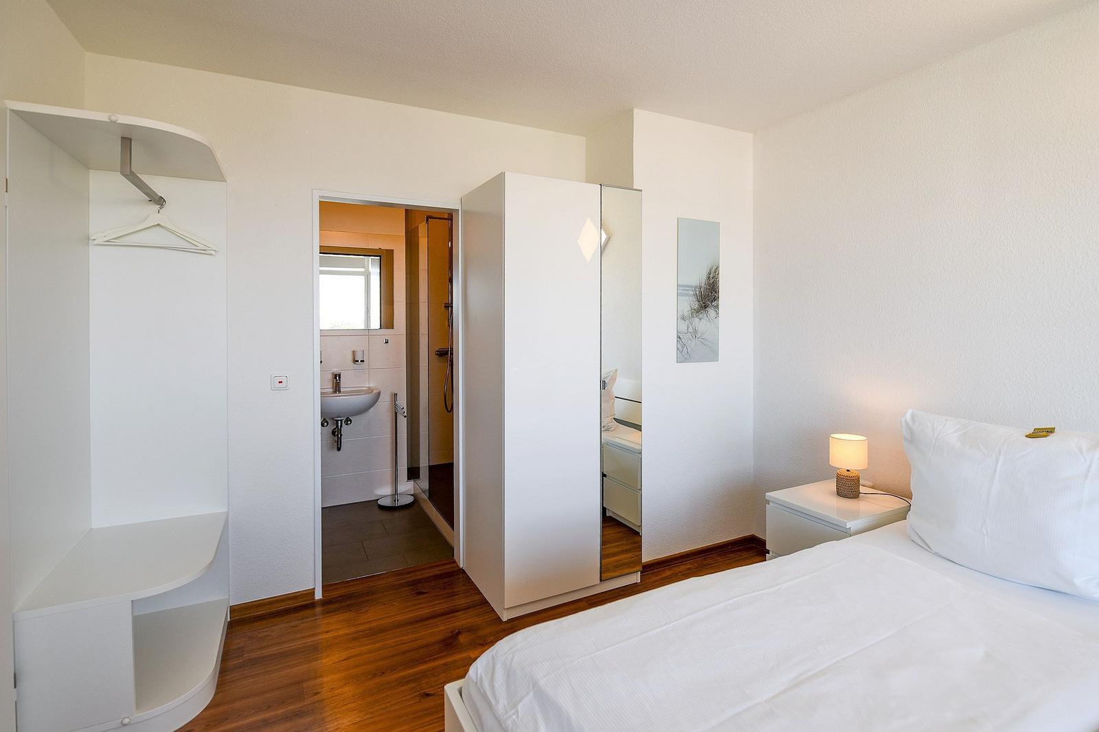 Schlafzimmer mit Bett, Nachttisch, Kleiderschrank und angrenzender Badewanne.