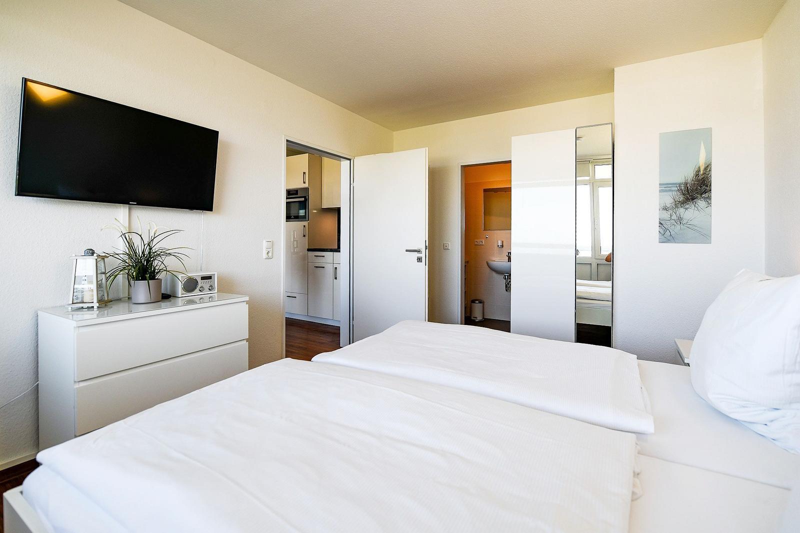Schlafzimmer mit Bett, Fernseher und Blick in Küche und Bad.