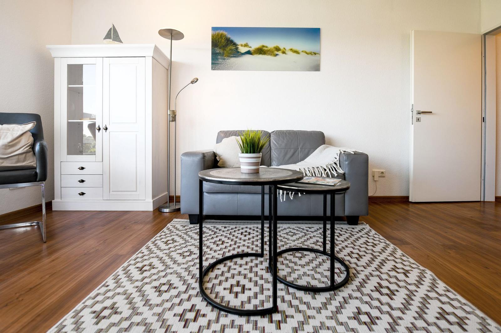 Wohnzimmer mit grauem Sofa, weißen Schränken und Holzboden.