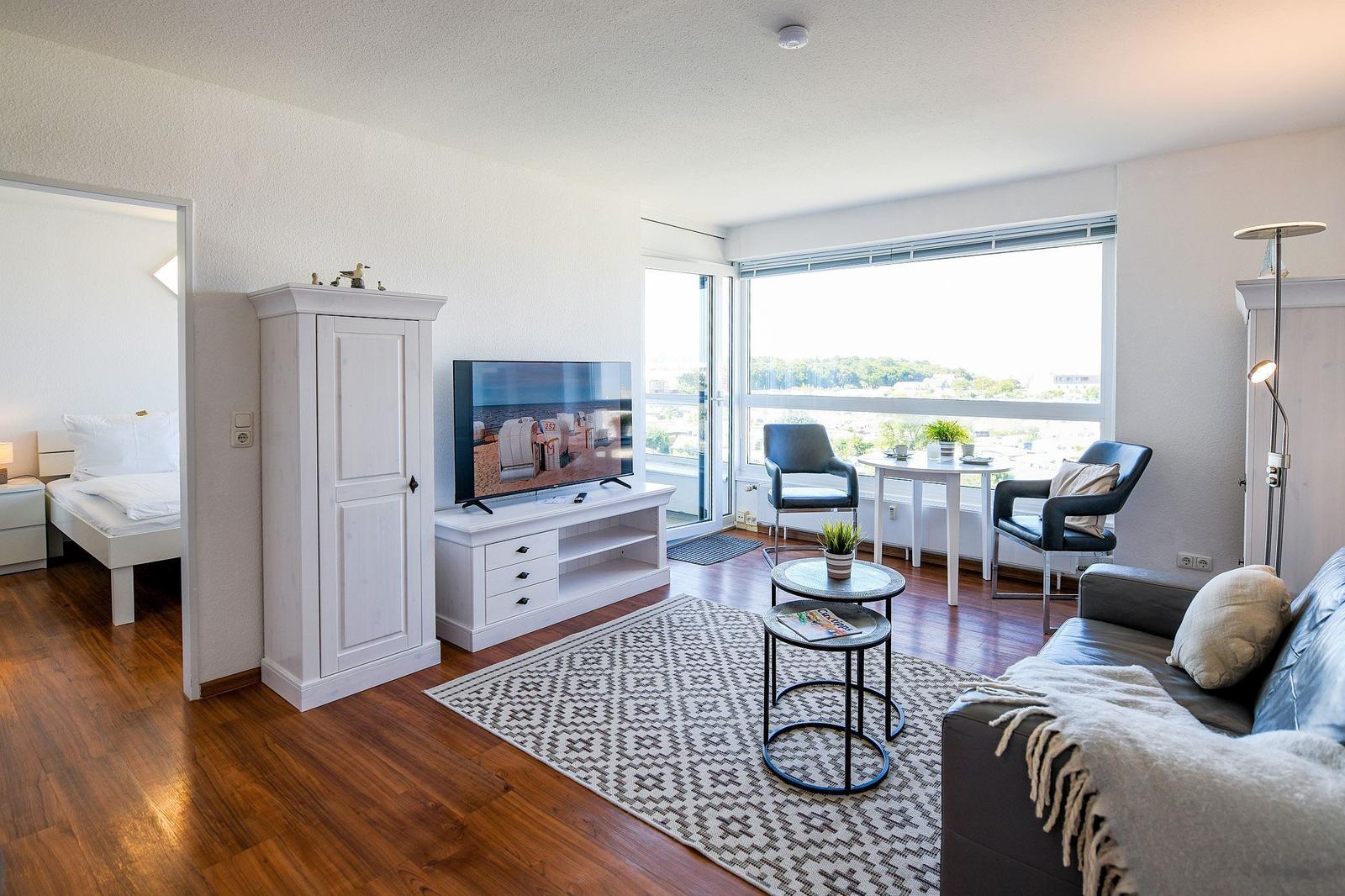 Wohnzimmer mit Sofa, Fernseher und Blick auf Balkon
