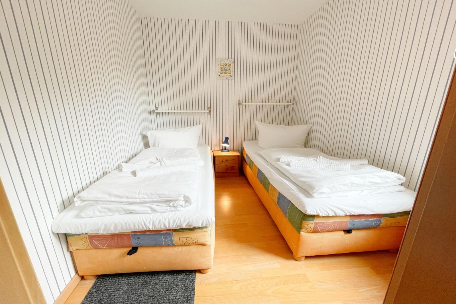 Zwei Einzelbetten mit weißen Bettwäschen und bunten Matratzenbezügen.