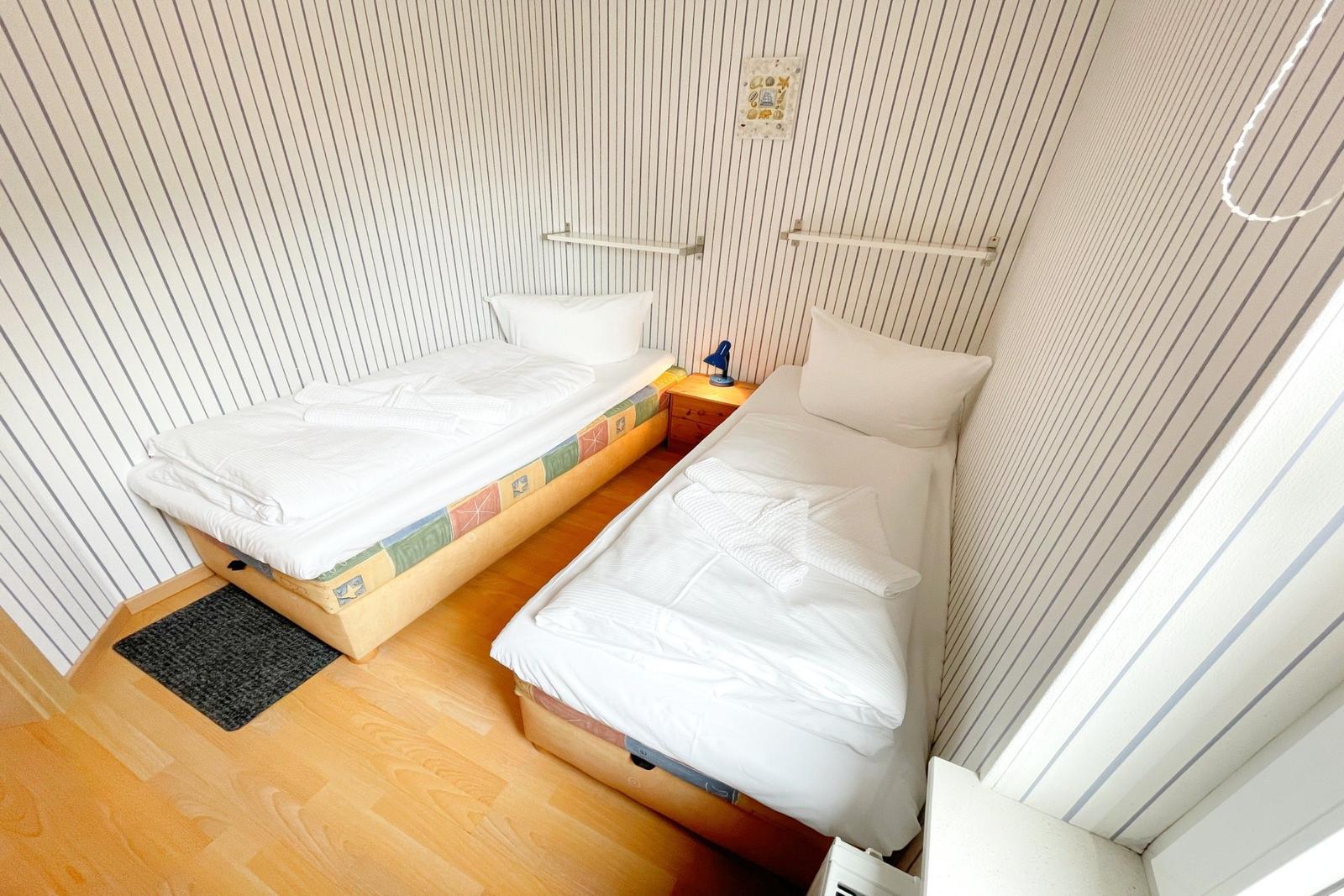 Zwei Einzelbetten mit weißen Bettwäschen und einem Nachttisch dazwischen.