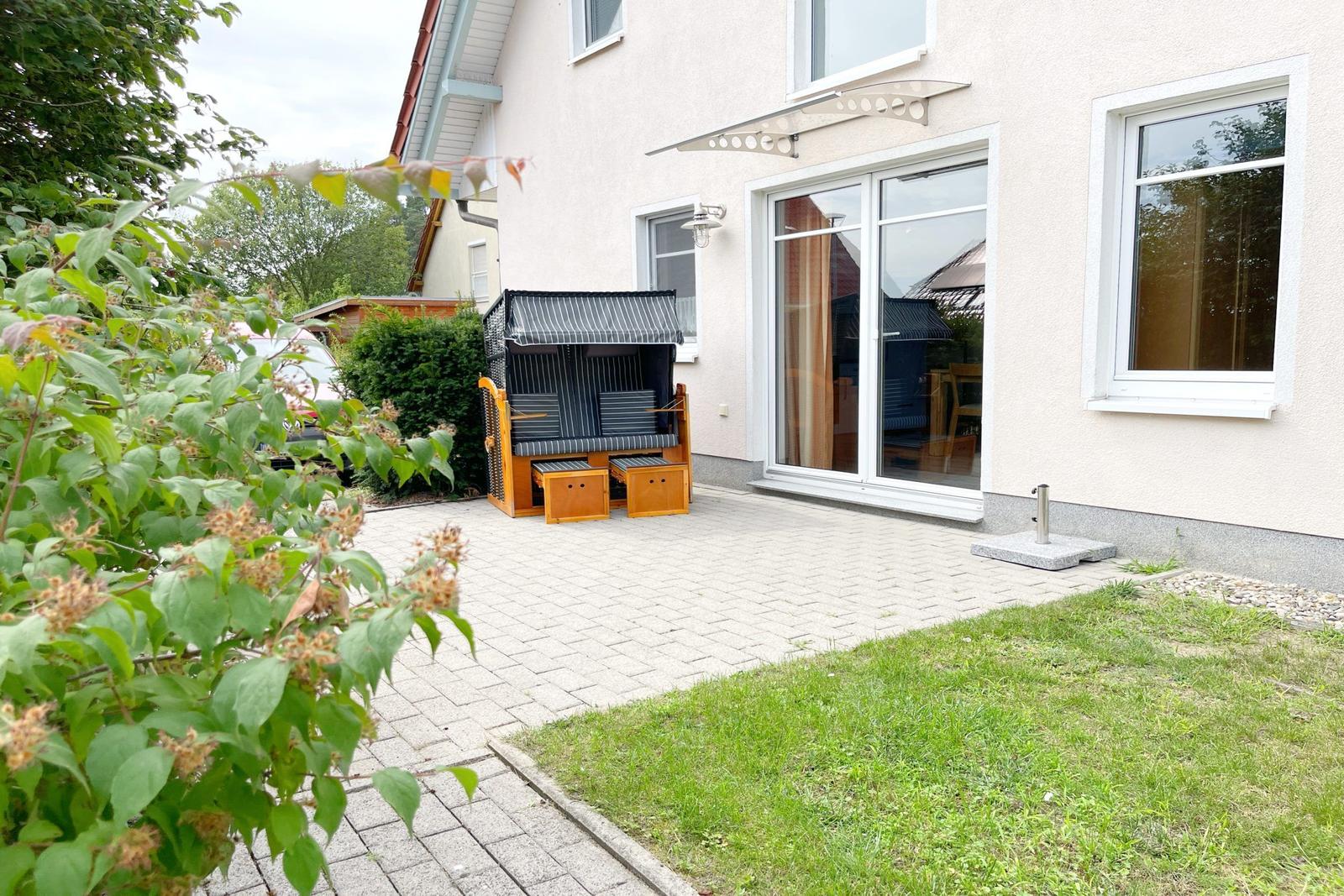 Hinterhof mit Holzliege, Pflaster und Grünfläche. Glastür führt ins Haus.