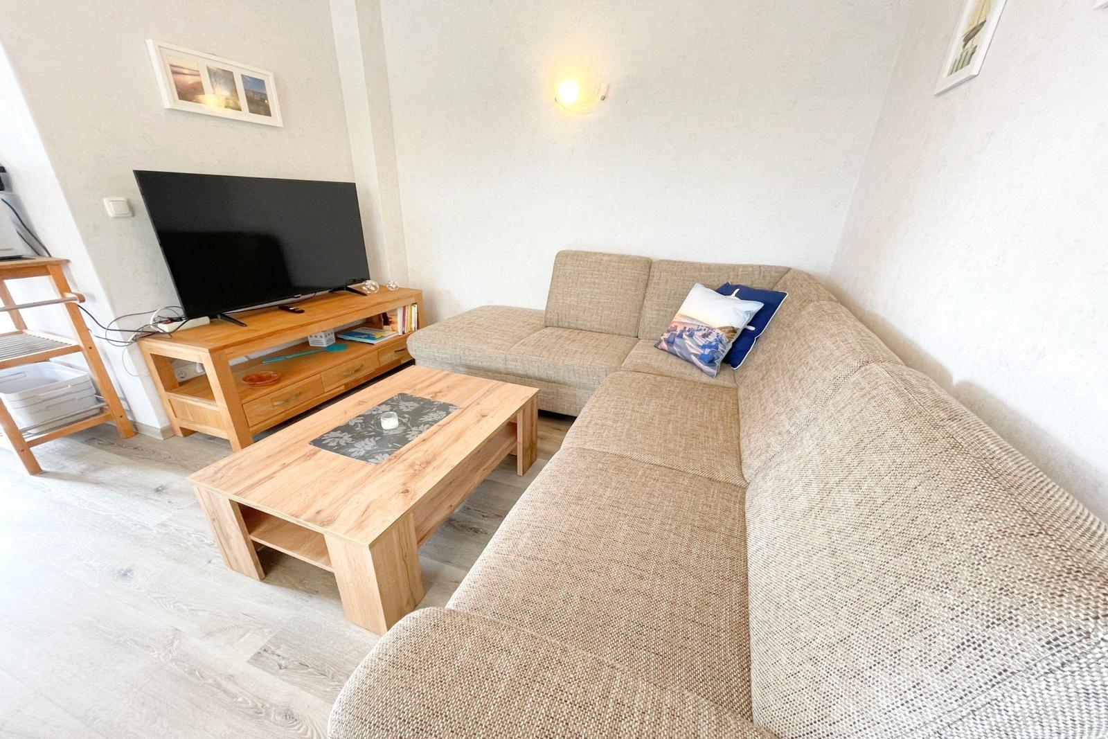 Wohnzimmer mit Ecksofa, Holztisch und Fernseher auf Holzregal.
