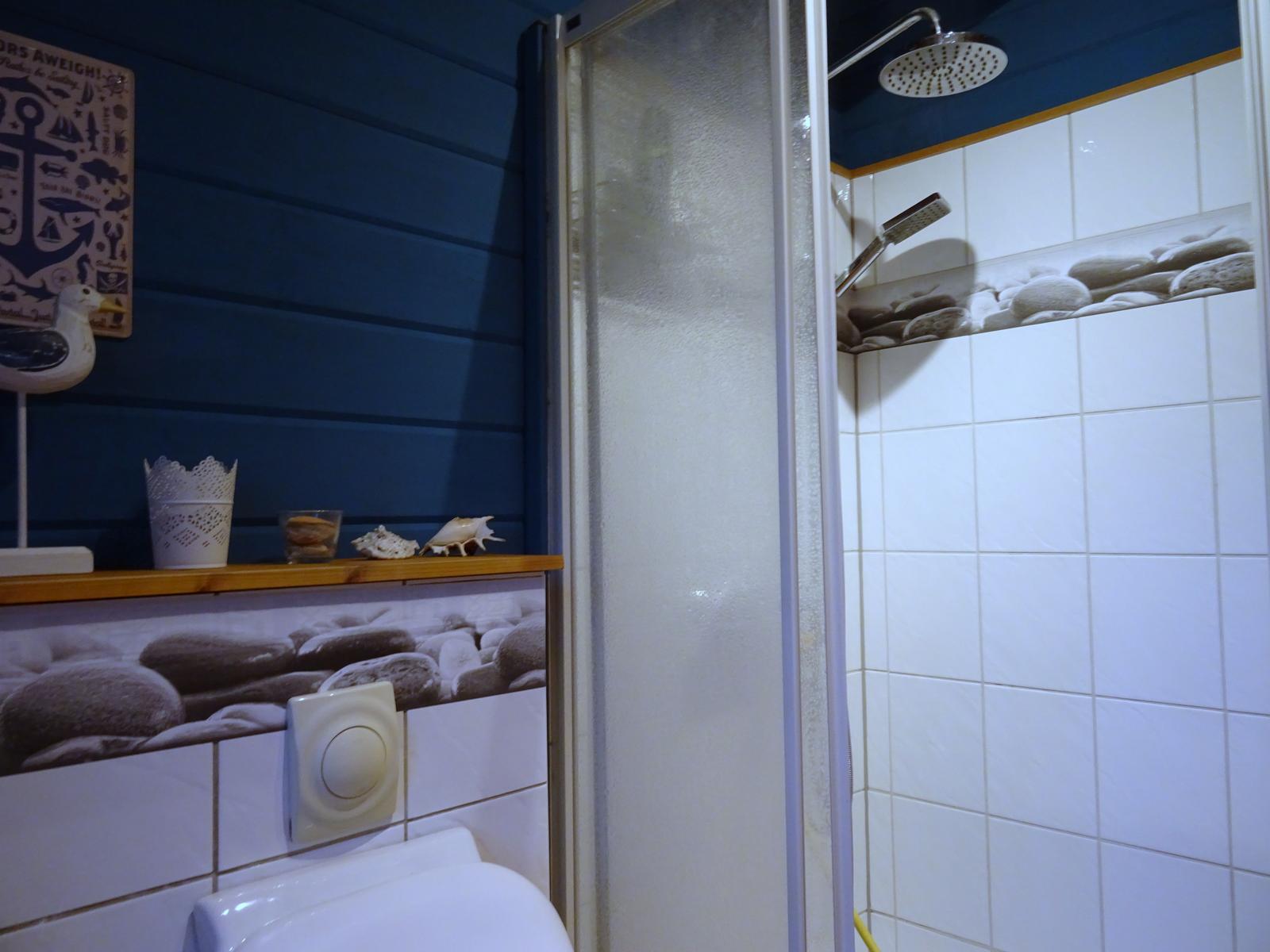 Badezimmer mit Dusche, Toilette und maritimen Dekorationen.