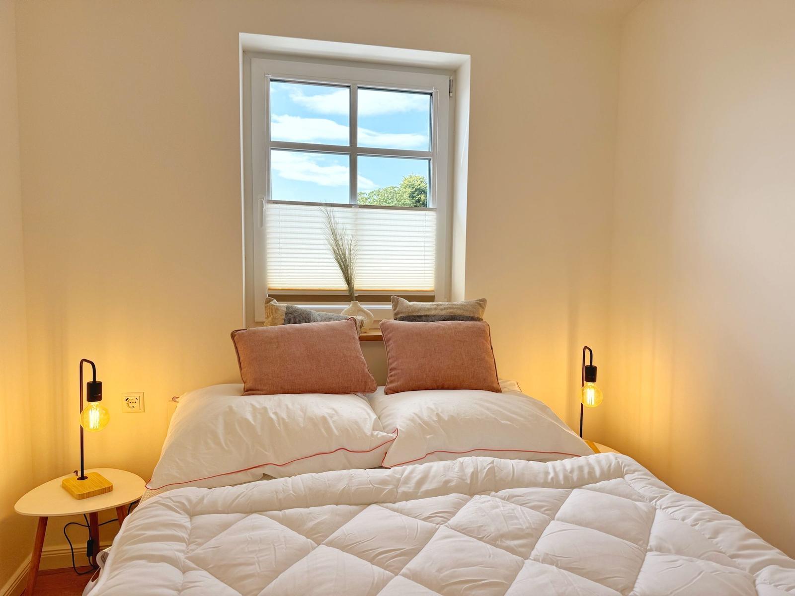 Doppelbett mit weißen Bettwäsche und zwei Nachttische mit Lampen.