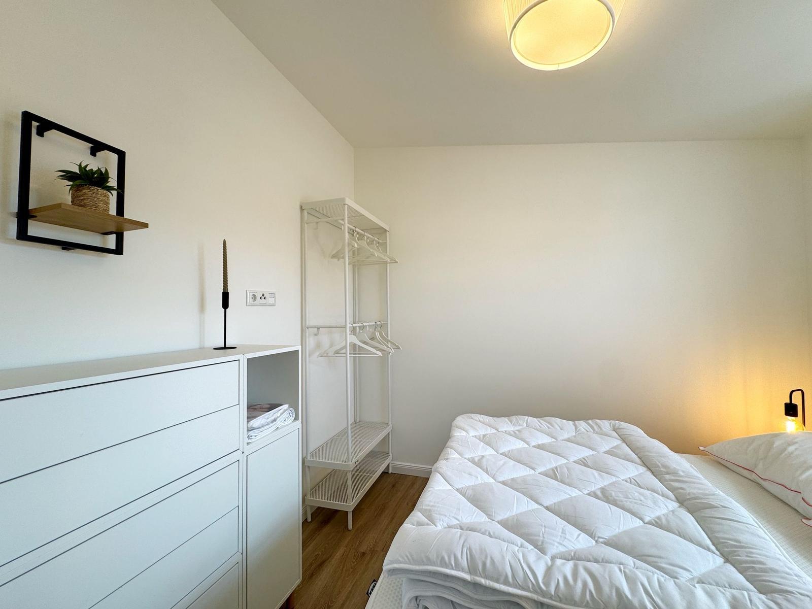 Schlafzimmer mit weißem Bett, Kleiderschrank und Garderobe.