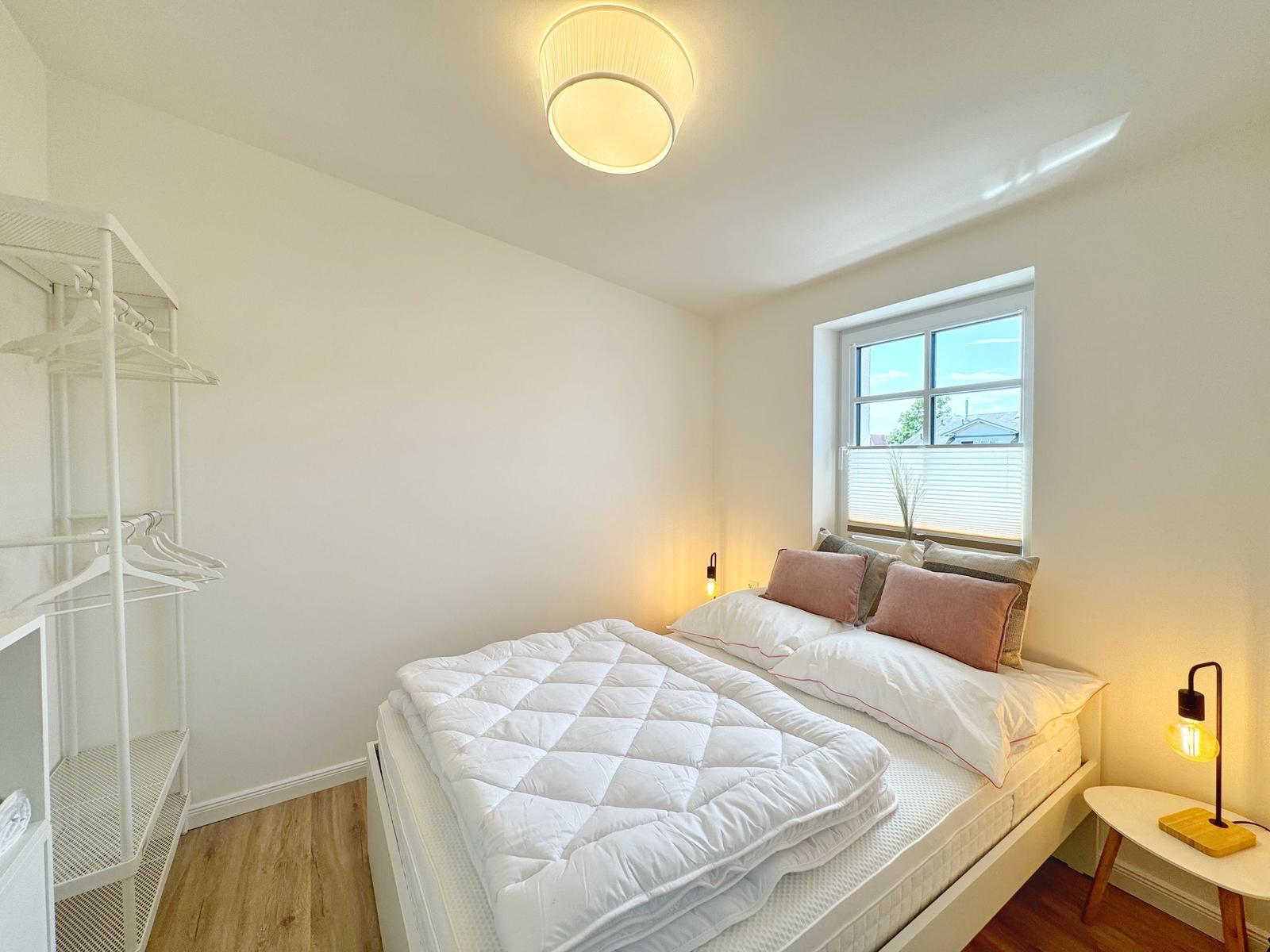 Schlafzimmer mit Bett, Kleiderschrank und Fenster.