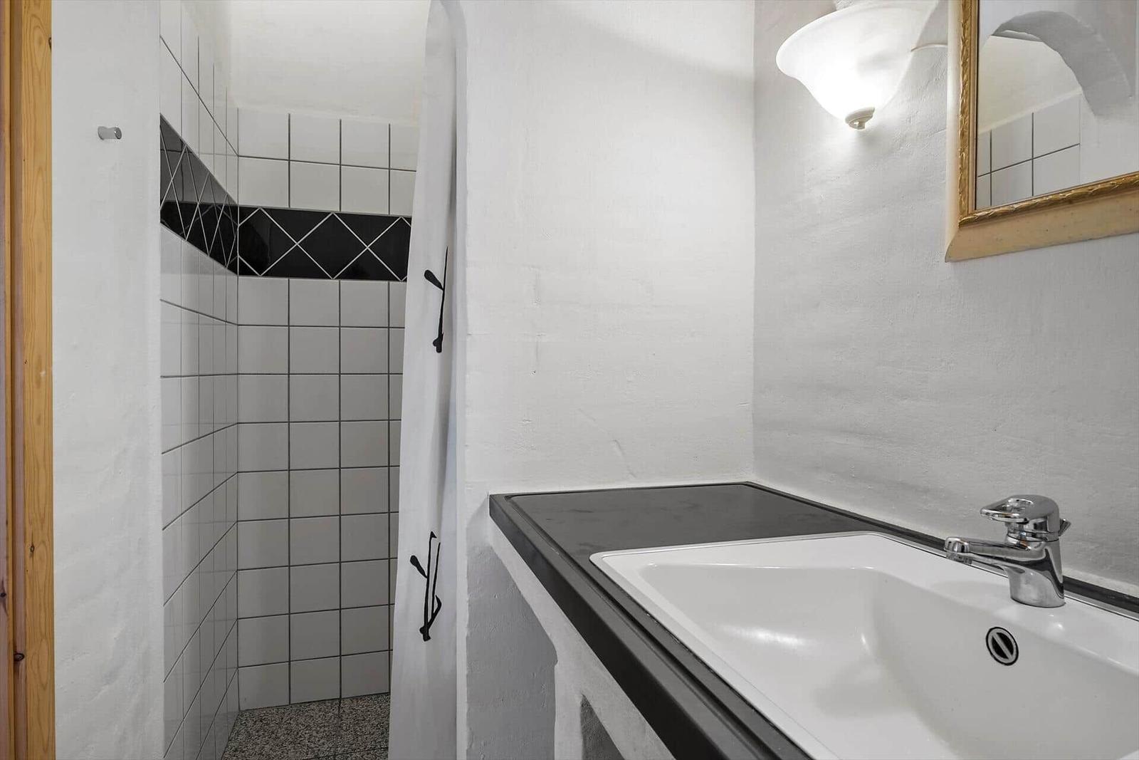 Bad mit Dusche, Waschbecken und Spiegel an der Wand.