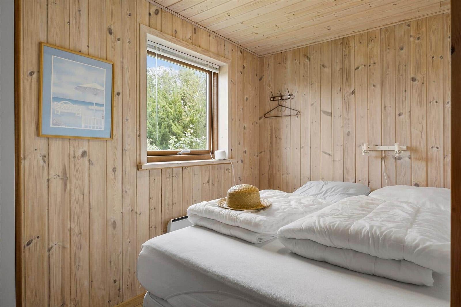 Schlafzimmer mit Holzwand, Bett und Fenster mit Blick auf Bäume.