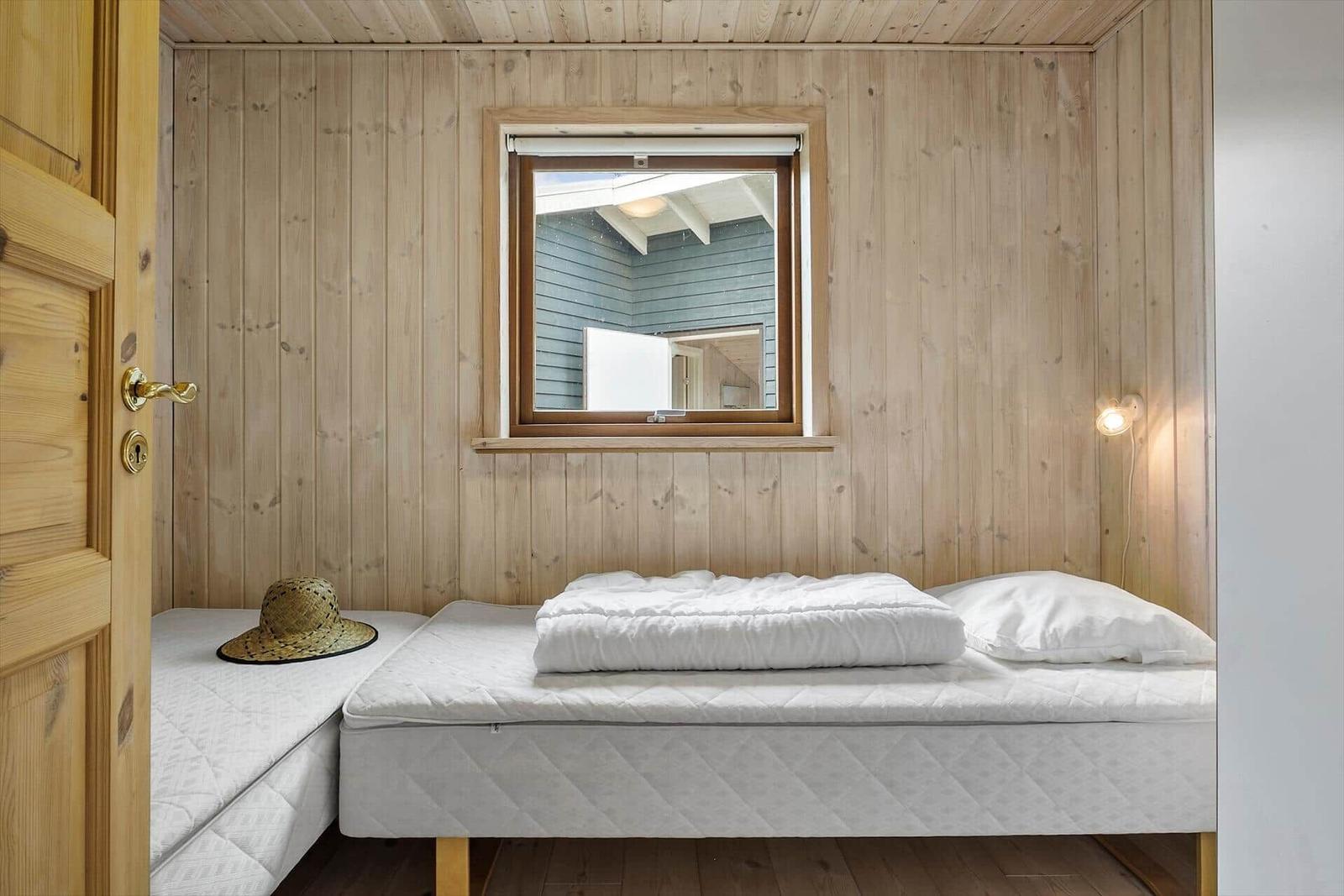 Schlafzimmer mit Holzwand, Bett und Fenster. Hut liegt auf Matratze.