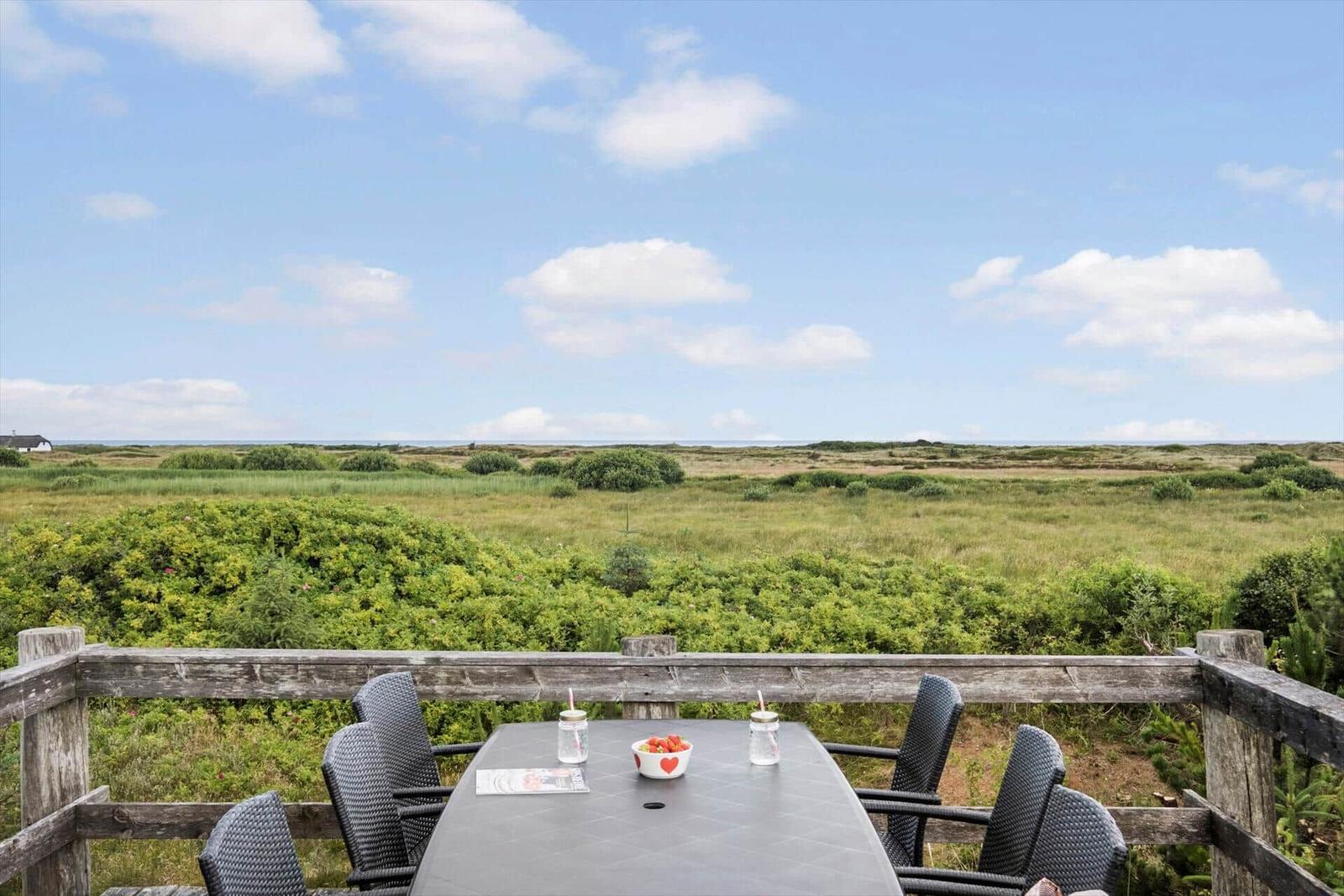 Terrasse mit Tisch und Stühlen bietet Blick auf grüne Landschaft und Horizont.