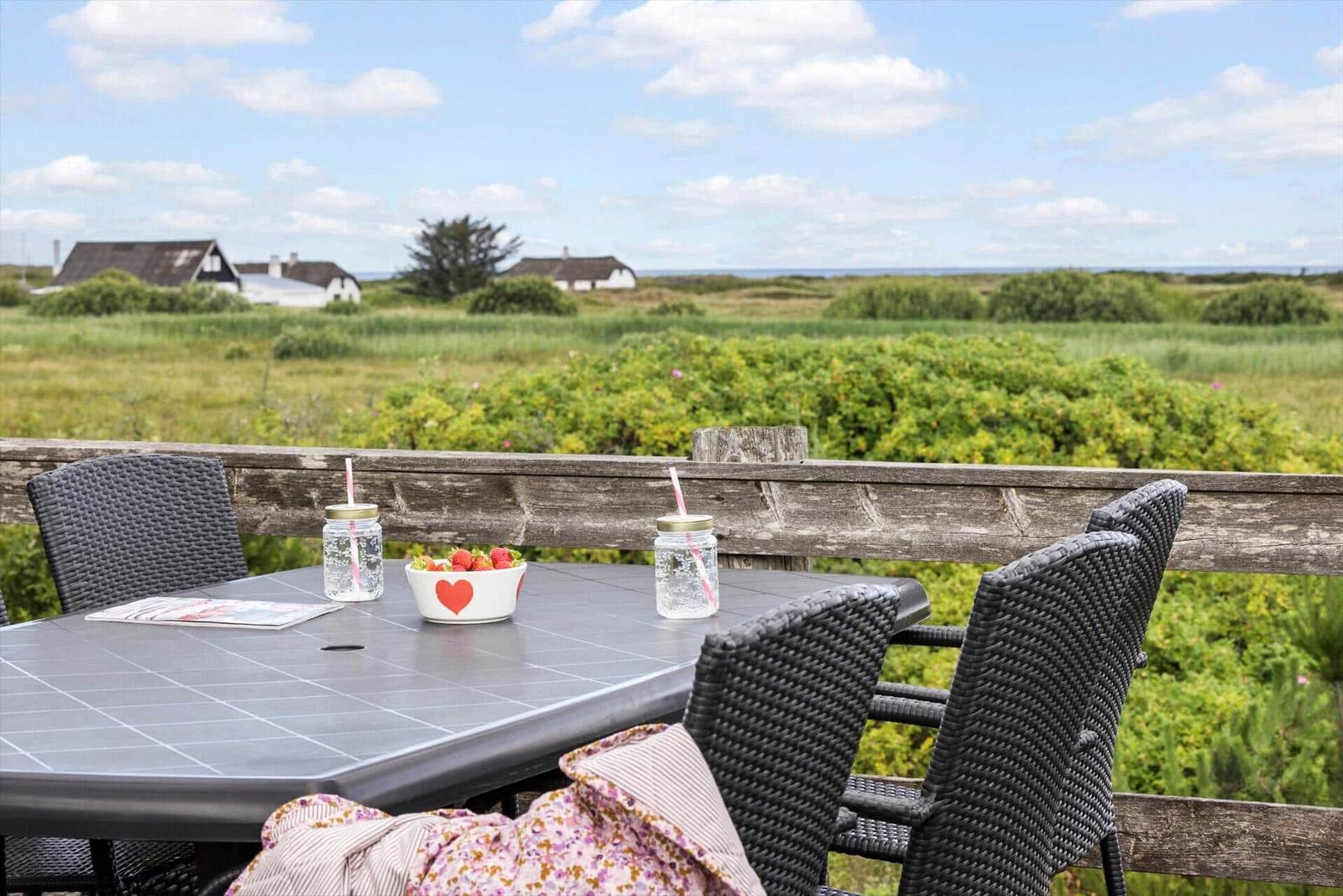 Terrasse mit Tisch, Stühlen und Blick auf Grünland und Häuser.