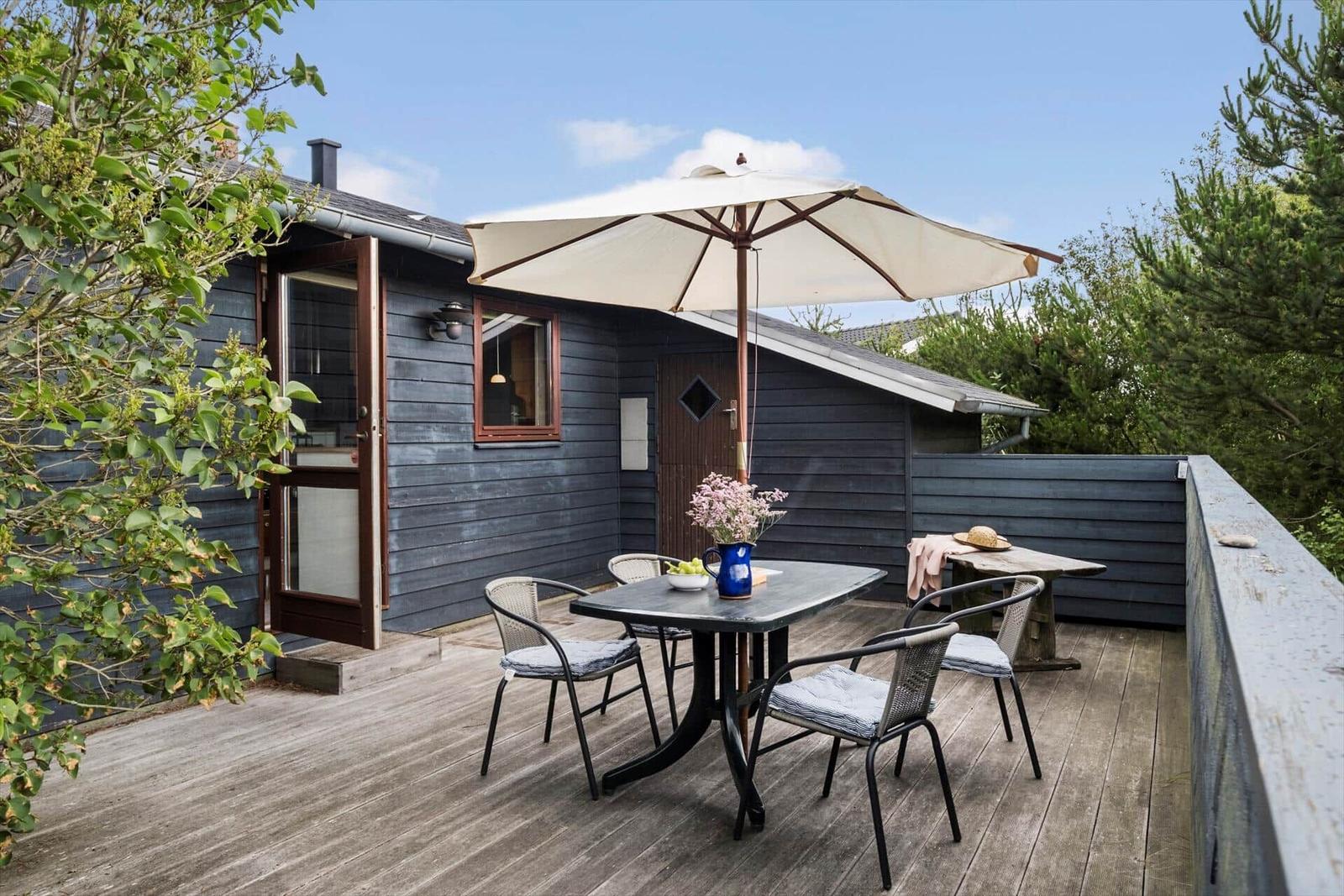 Terrasse mit Tisch, Stühlen und Sonnenschirm vor einem Holzhaus.