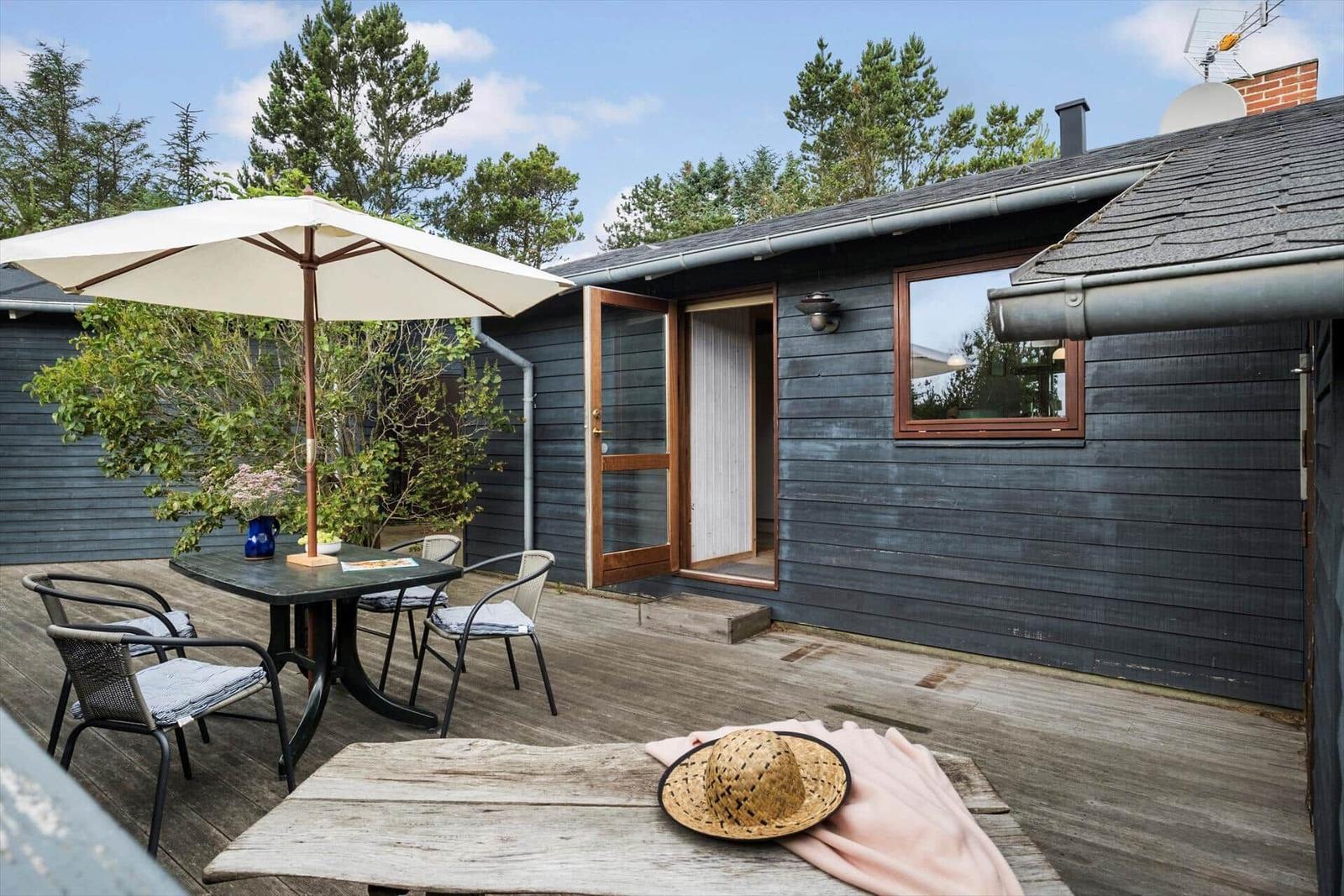 Terrasse mit Tisch, Stühlen und Sonnenschirm vor einem Haus mit dunklem Holzschindeldach.