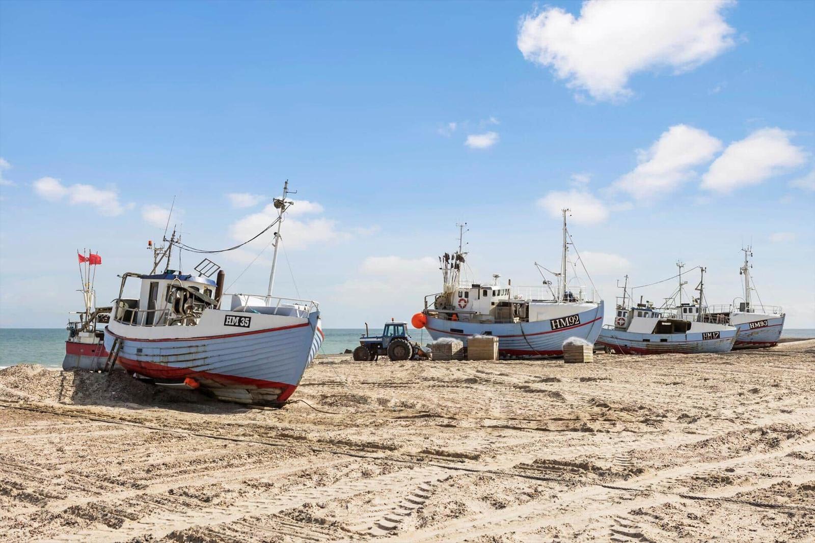 Fischerboote liegen auf dem Strand, ein Traktor steht daneben.