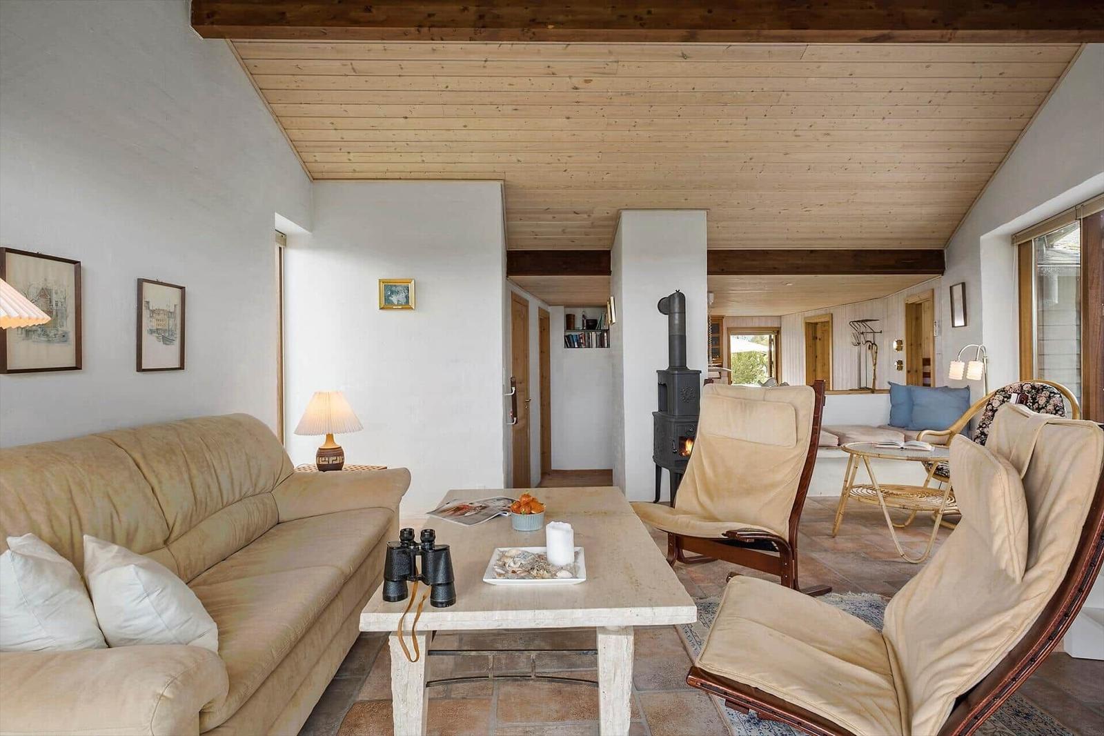 Wohnzimmer mit Sofa, Sesseln und Kaminofen. Holzdecke und Terrakottaboden.