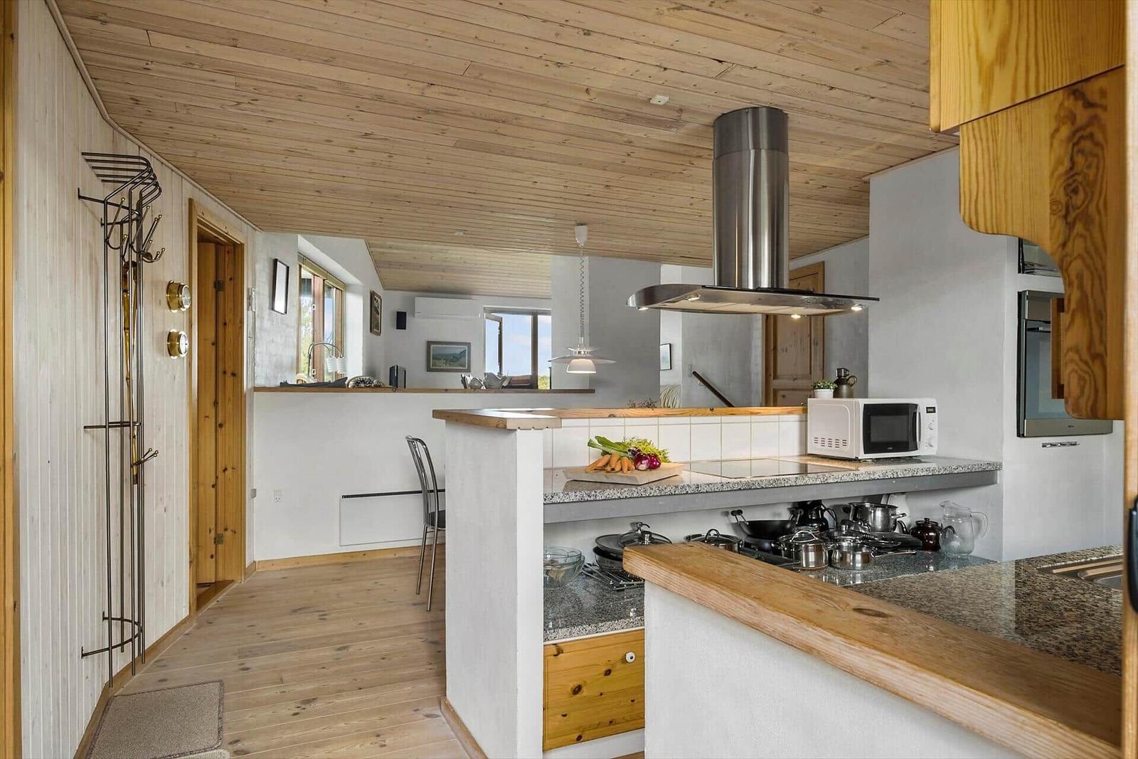Küche mit Holzboden, -decke und -schränken. Esstisch, Herd und Dunstabzug.