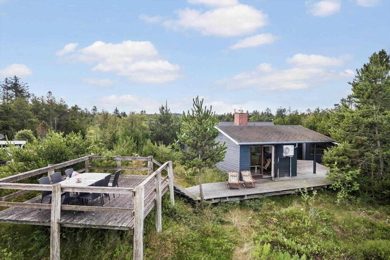 Haus mit Terrasse, Grillplatz und Blick auf Wald.