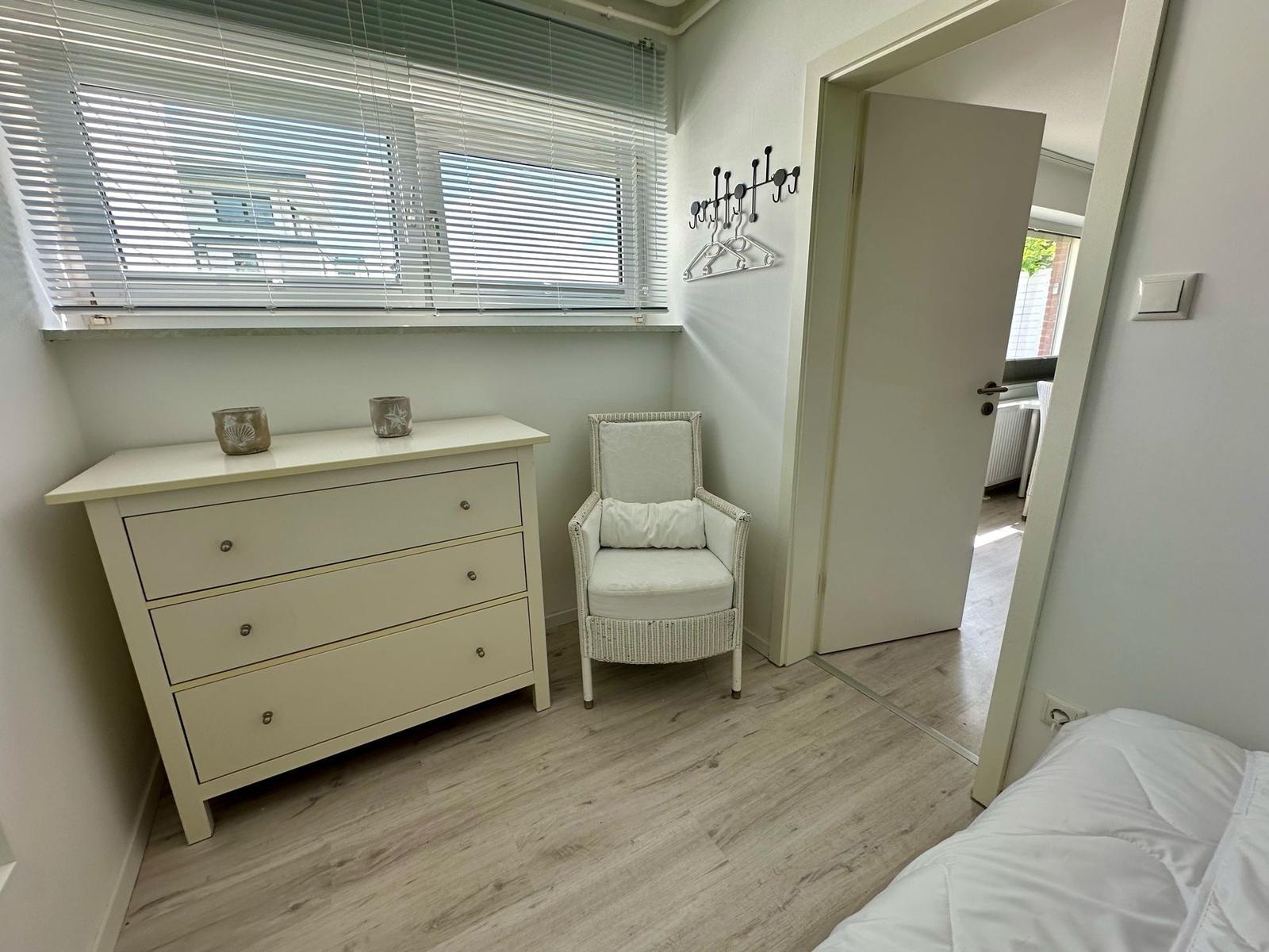 Schlafzimmer mit Schrank, Sessel und Blick auf angrenzenden Raum.