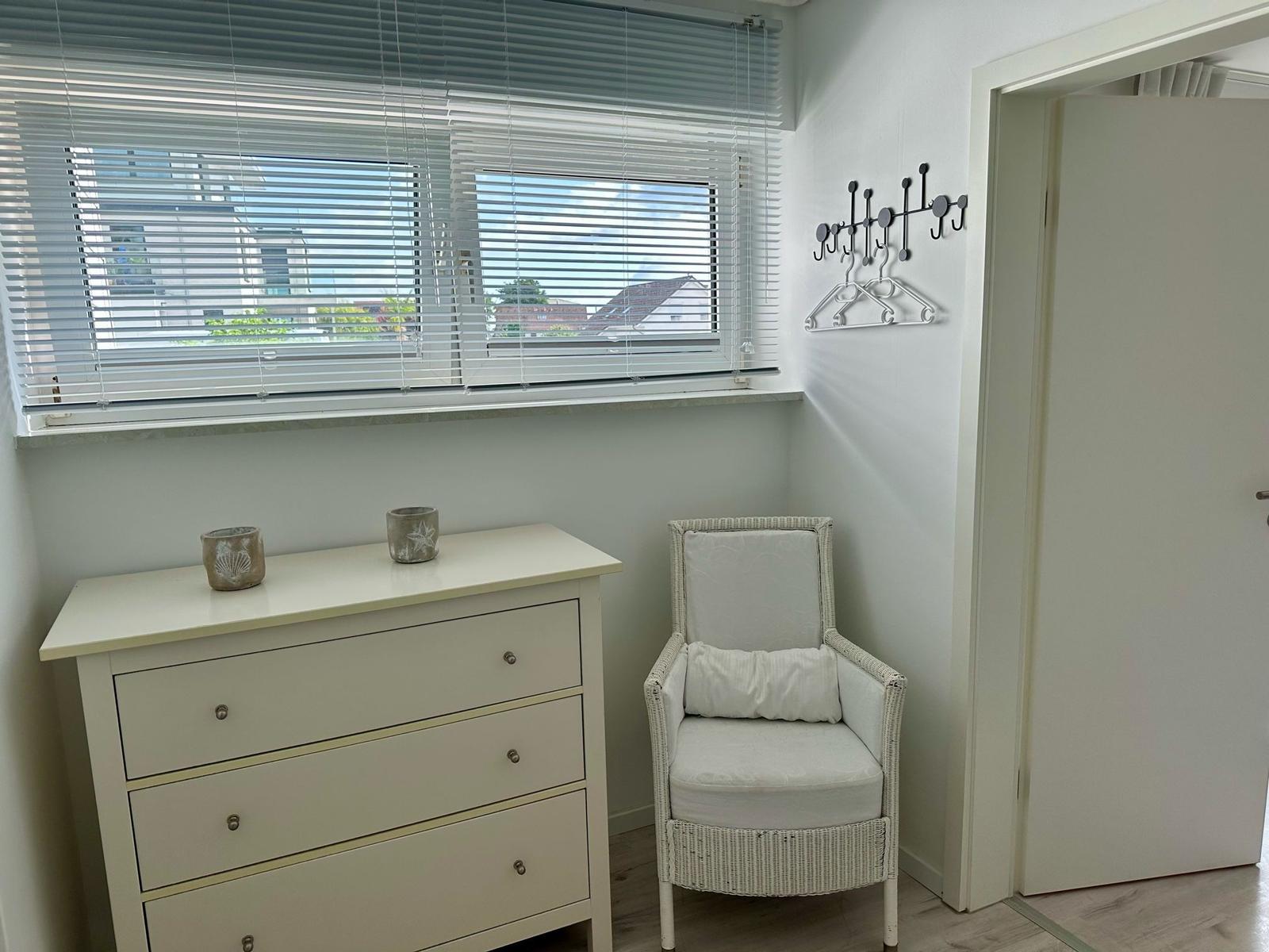 Schlafzimmer mit Schrank, Sessel und Fenster mit Jalousie.