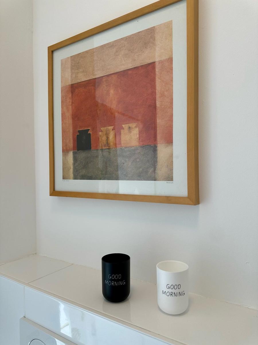 Ein Bild mit Holzrahmen hängt über zwei Tassen mit der Aufschrift GOOD MORNING.