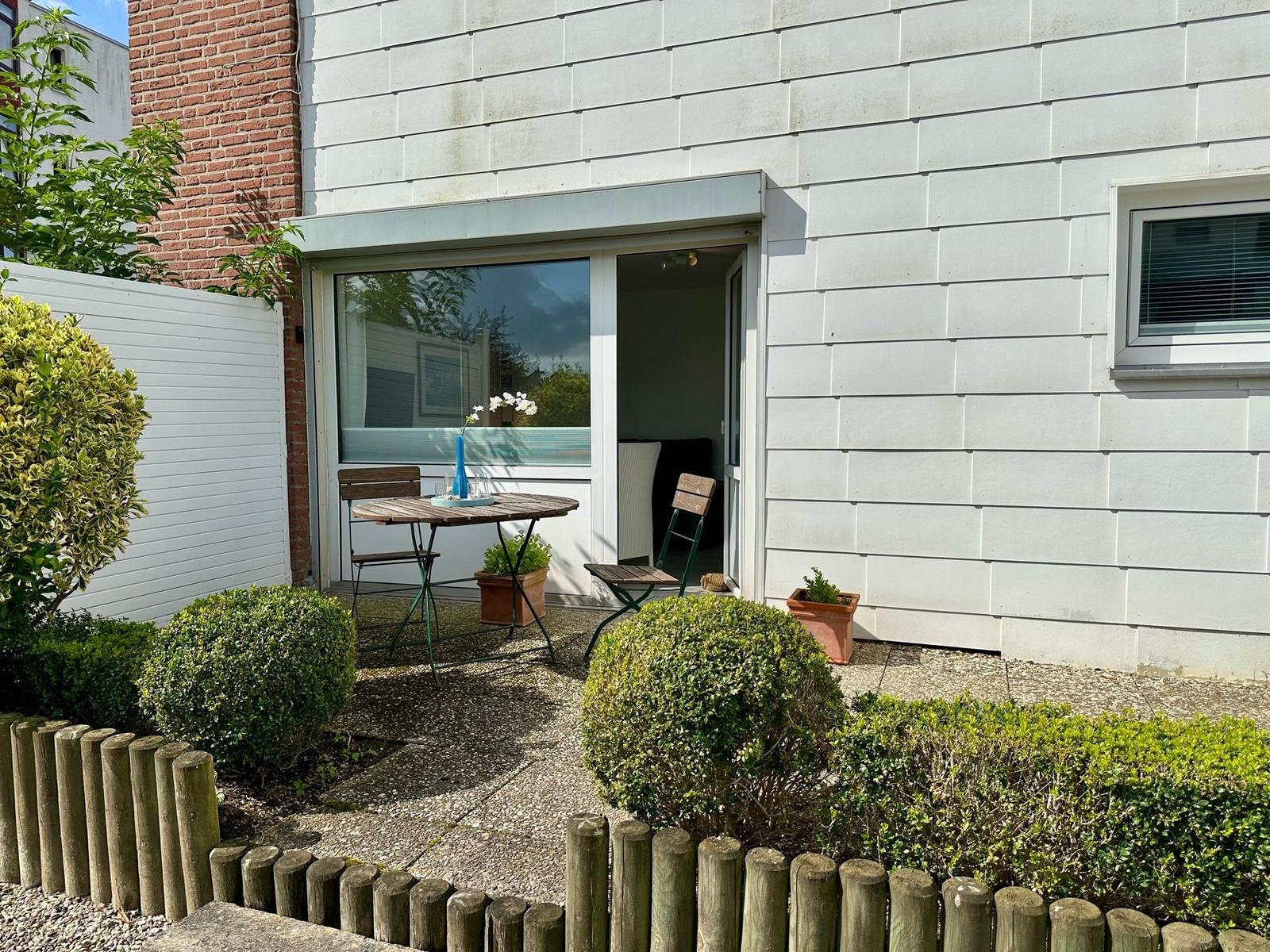 Hinterhof mit Tisch, Stühlen und Pflanzen. Durchgehende Glastür zum Innenraum.