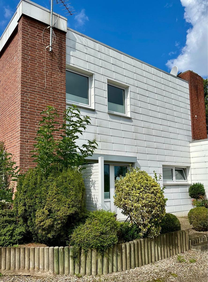 Modernes Haus mit weißen Fassaden, roten Ziegelsteinen und grüner Umgebung.