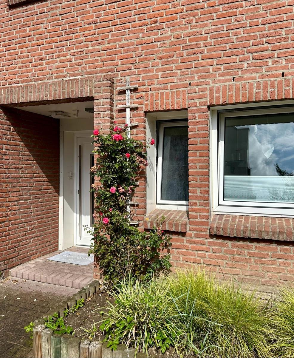 Rotes Backsteinhaus mit Eingang, Fenster und Rosenstrauß.
