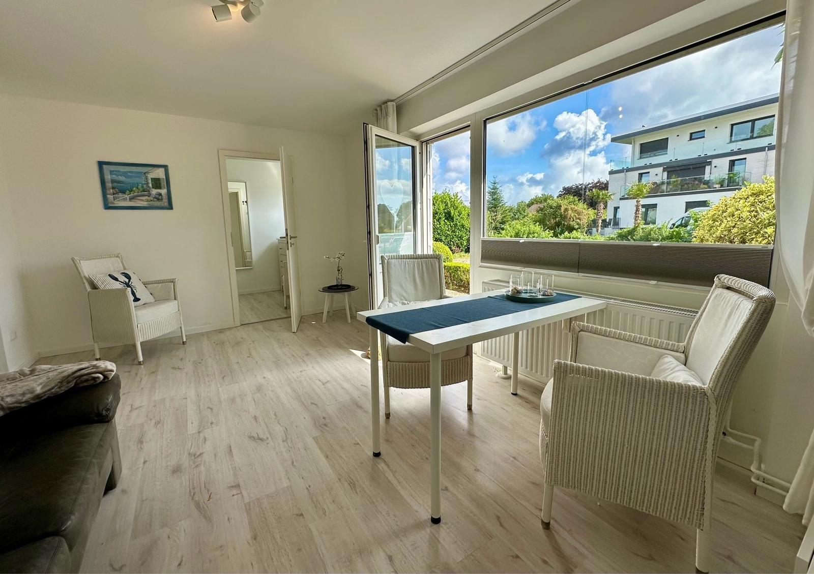 Essbereich mit Tisch und Stühlen. Große Fenster mit Blick auf Garten und Haus.